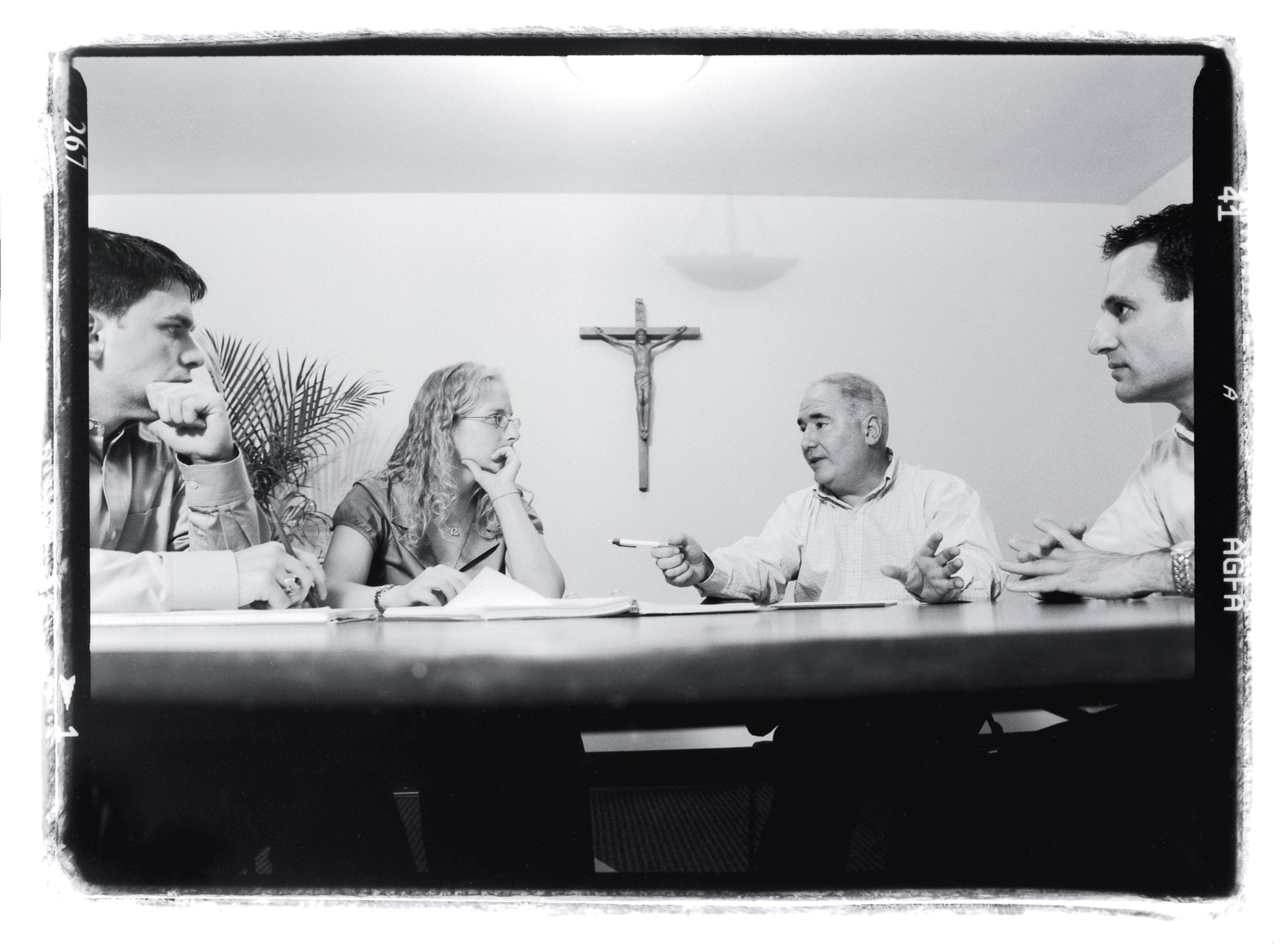 Four people sitting at a table with a cross hanging in the background