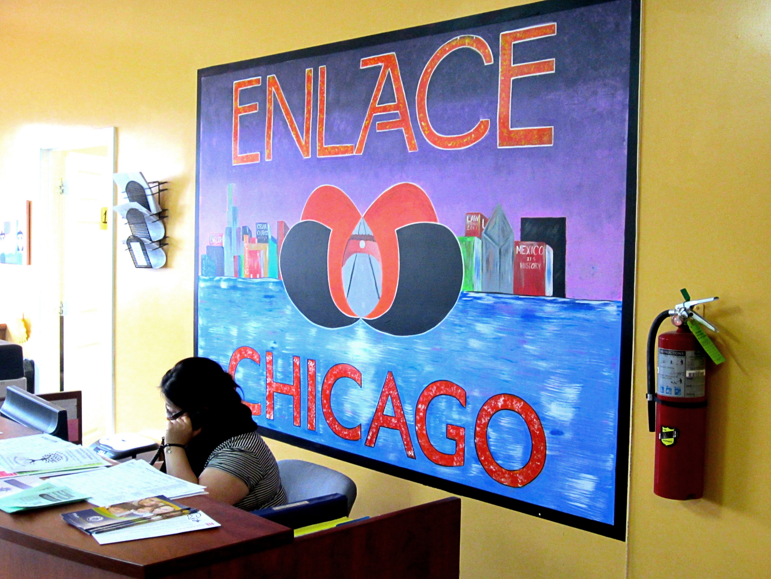 Mural with the words 'Enlace Chicago' on the wall behind a woman sitting at a desk