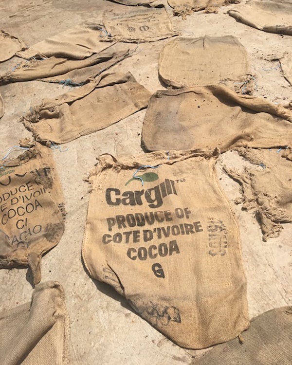 Bags used to collect and ship cocoa beans laying on the ground. Printed on the bags: 