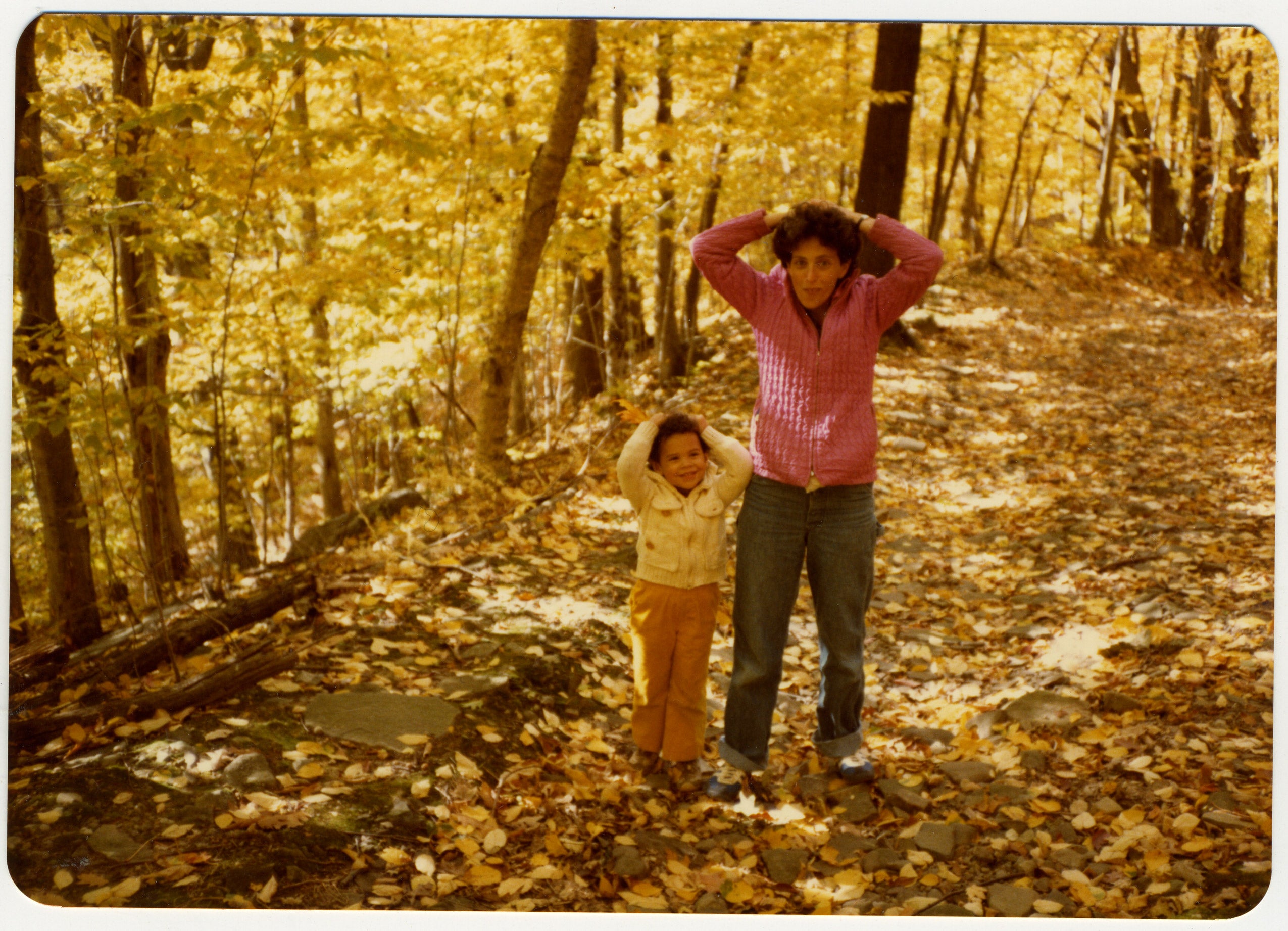 A woman and daughter on a forest trail covered with fall leaves