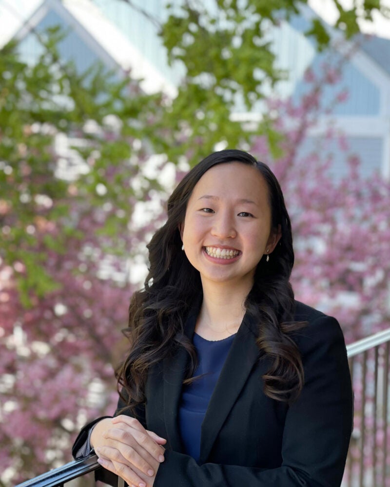 Woman with blue blazer and blue shirt and long black hair in front of pink flowering bush