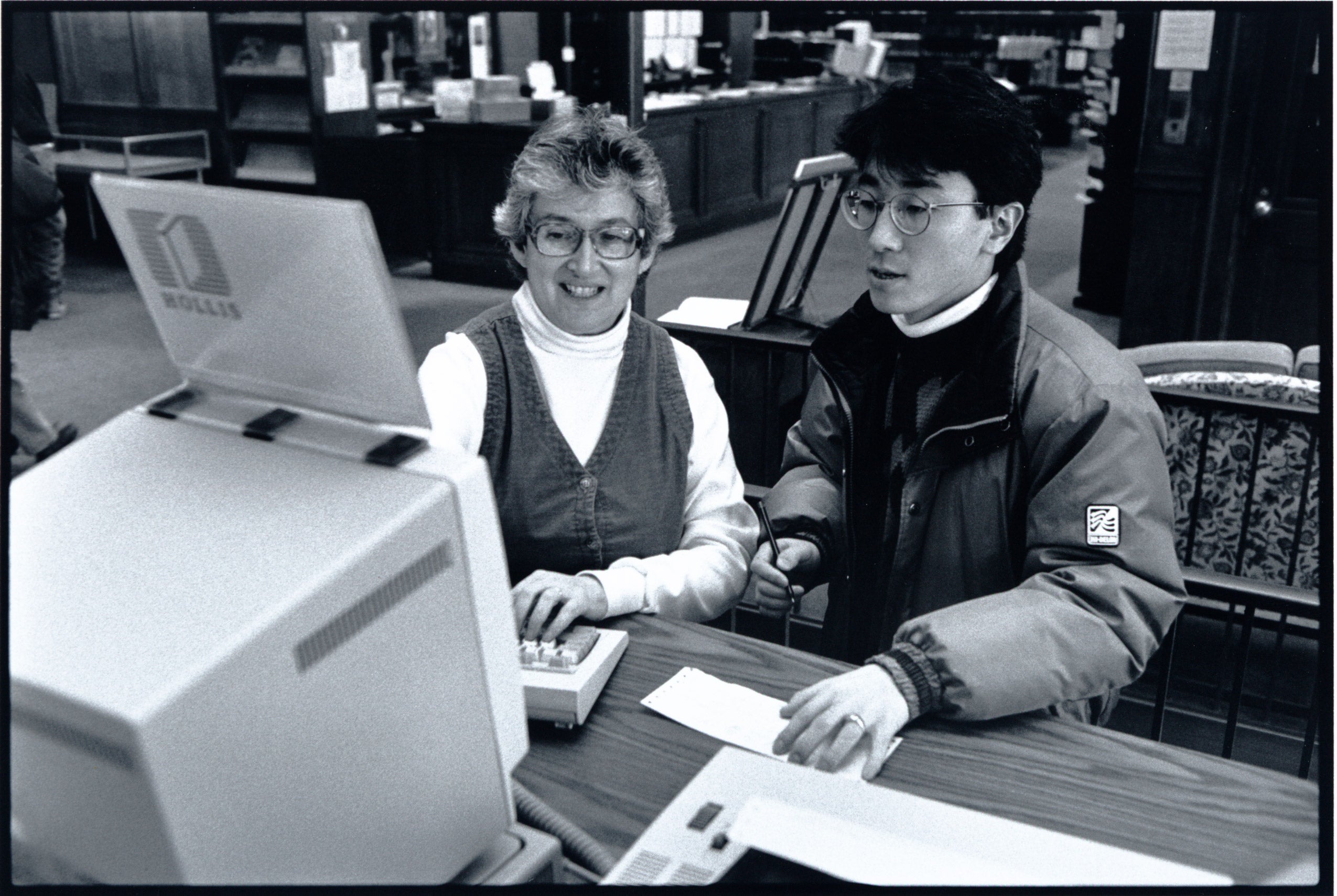 Woman helping a young man at at computer terminal in a library