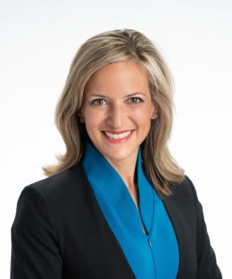 Smiling woman with blonde hair wearing a navy blue jacket and blue blouse
