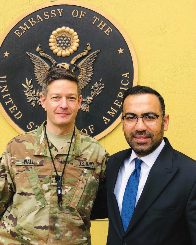 Andru Wall dressed in military uniform and classmate Andru Wall stand in from the the Seal of the Embassy of the the United States in Kabul