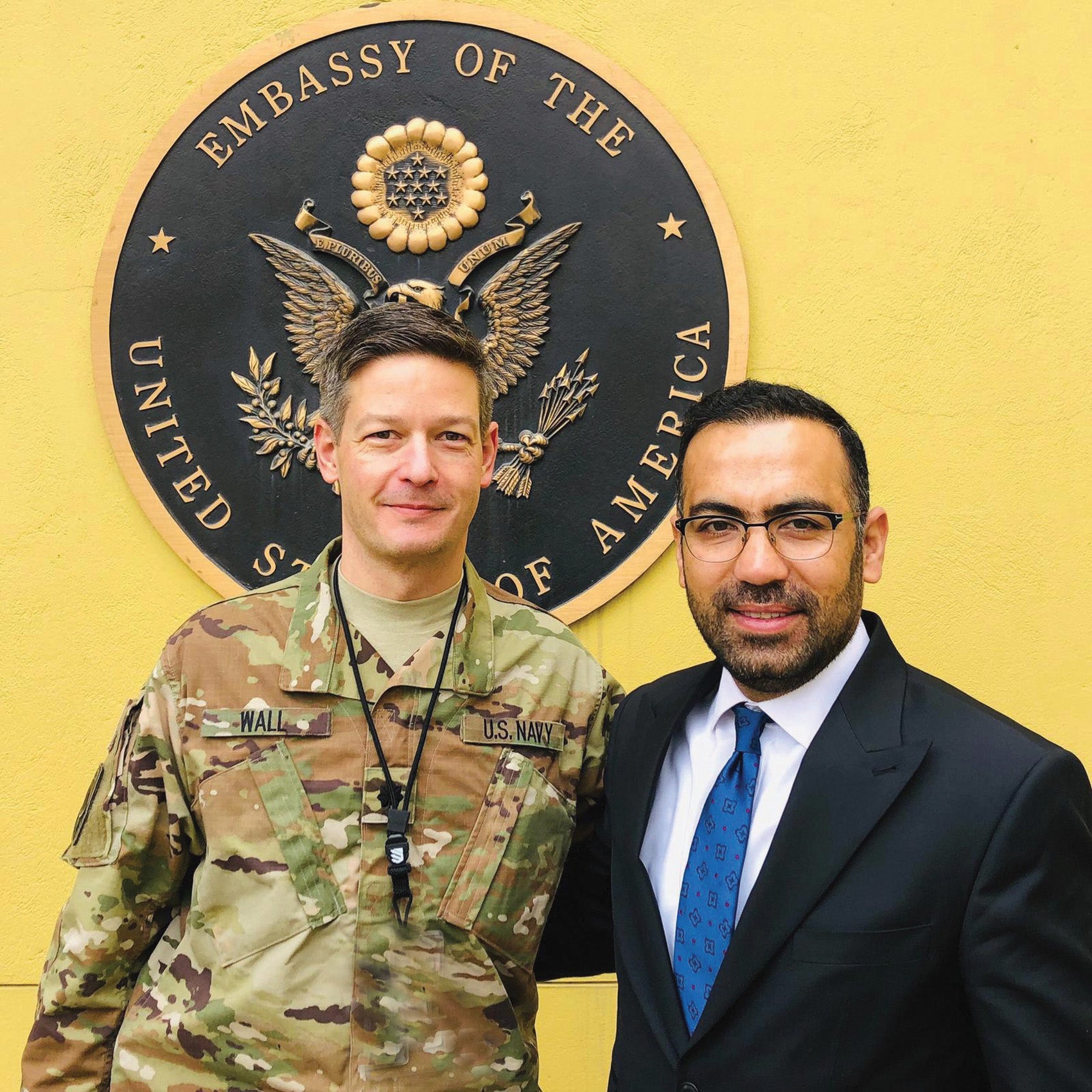 Andru Wall dressed in military uniform and classmate Andru Wall stand in from the the Seal of the Embassy of the the United States in Kabul