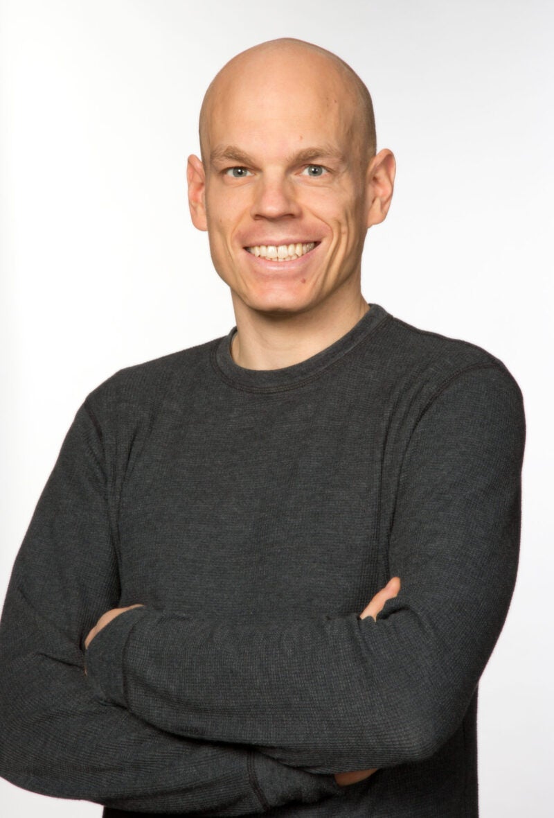 Holger Spamann smiling at the camera with arms folded in a longsleeve black shirt