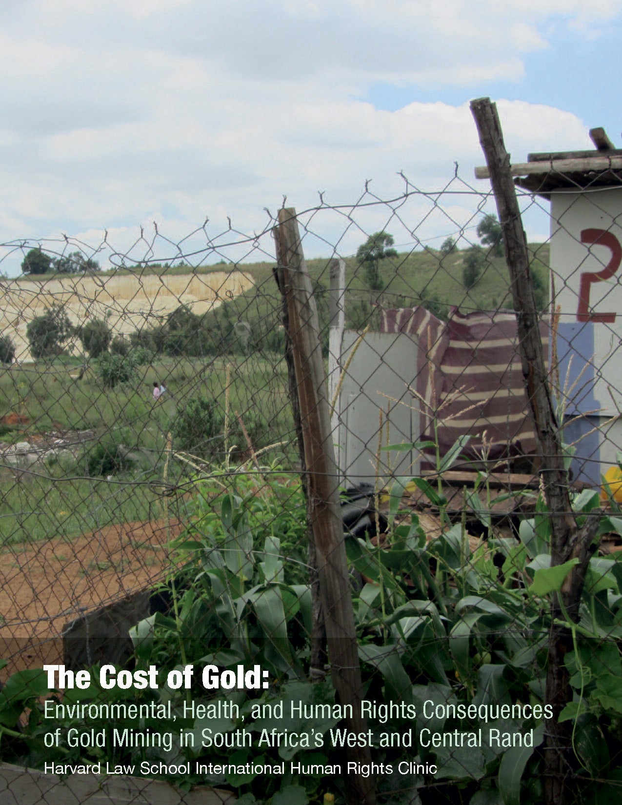 The Cost of Gold cover, a view of a shack and hillside from behind an old chainlink fence