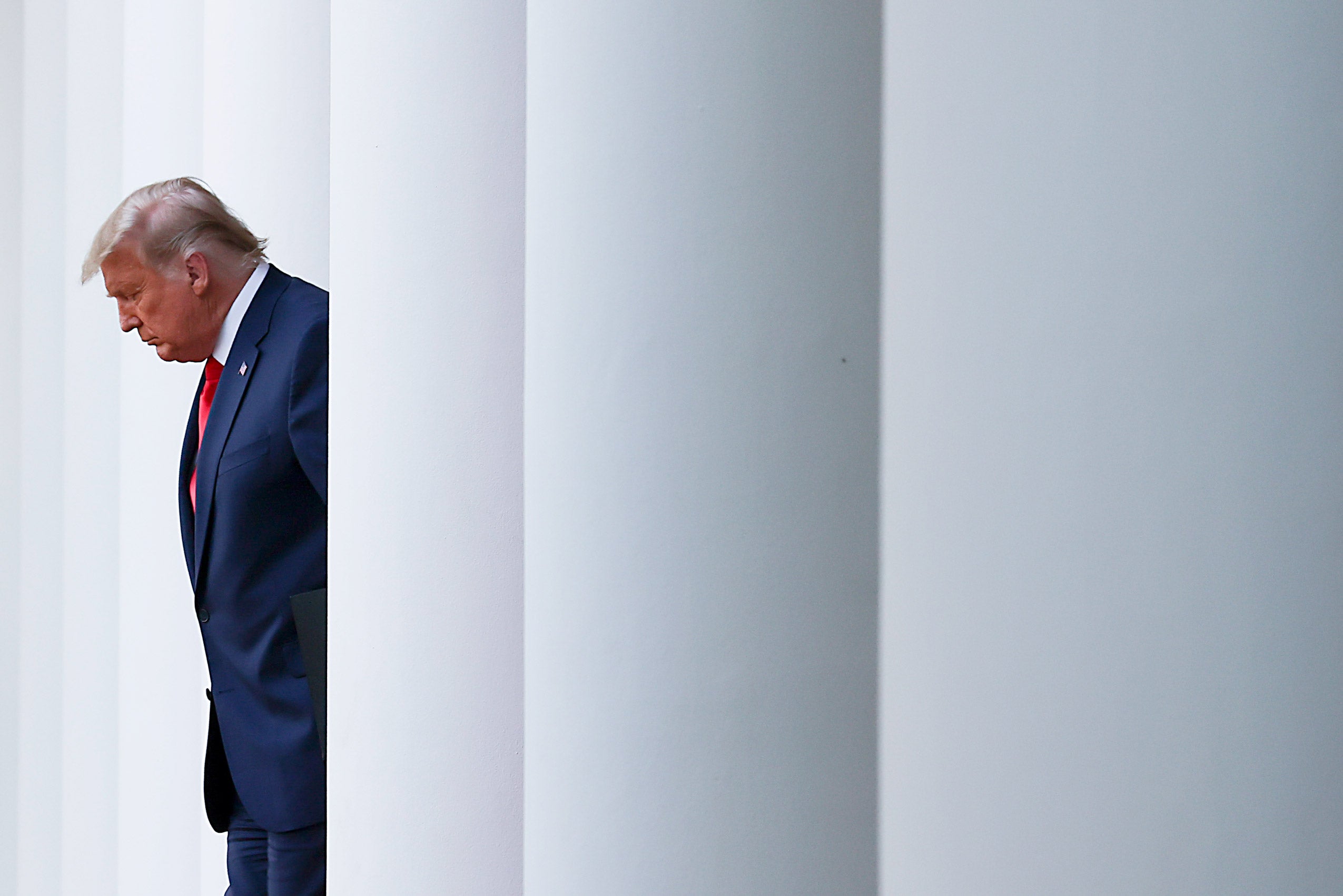 President Donald Trump standing between large white columns of the White House.