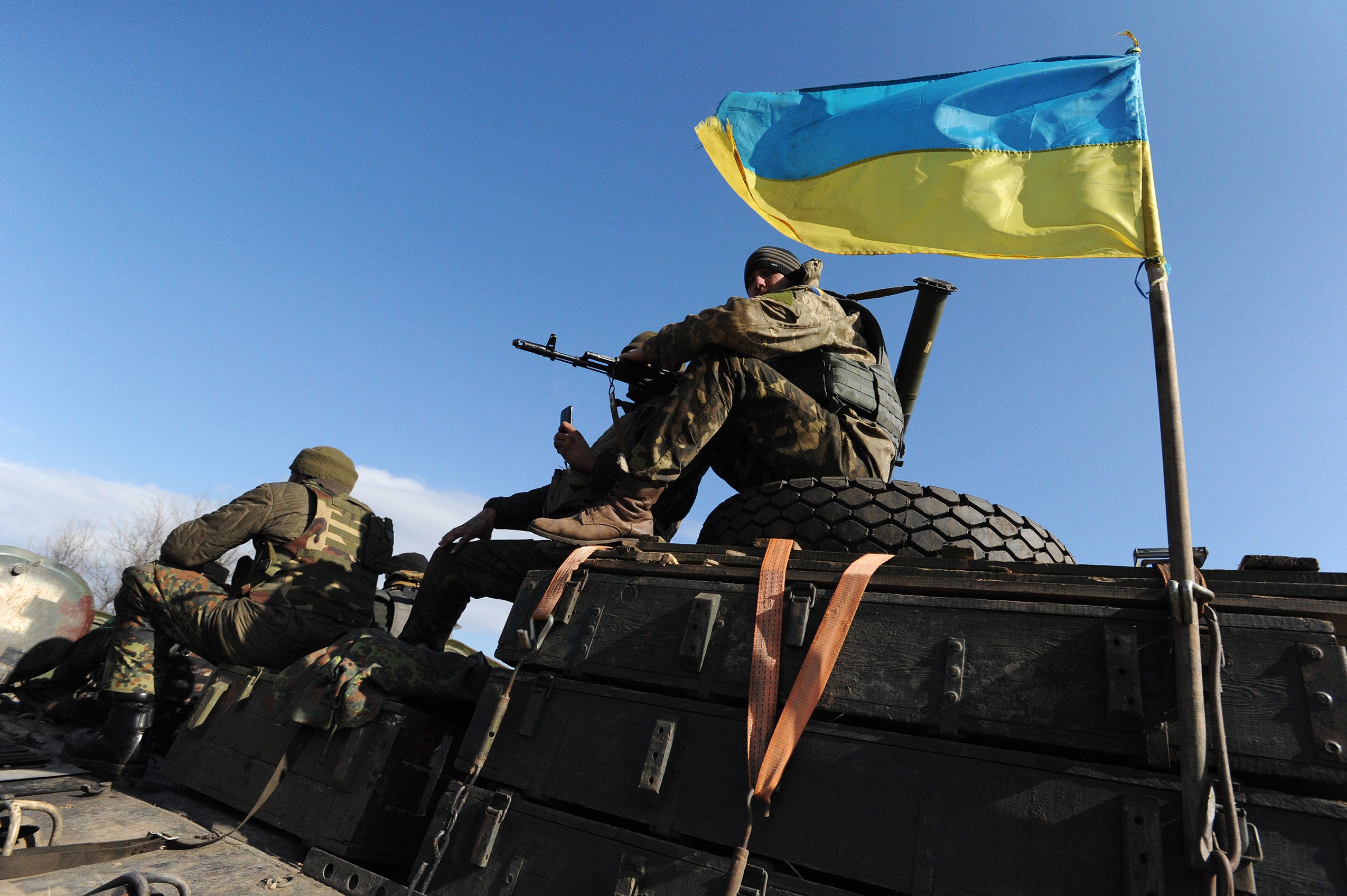 A soldier sitting on top of a military tank that is flying the Ukranian flag