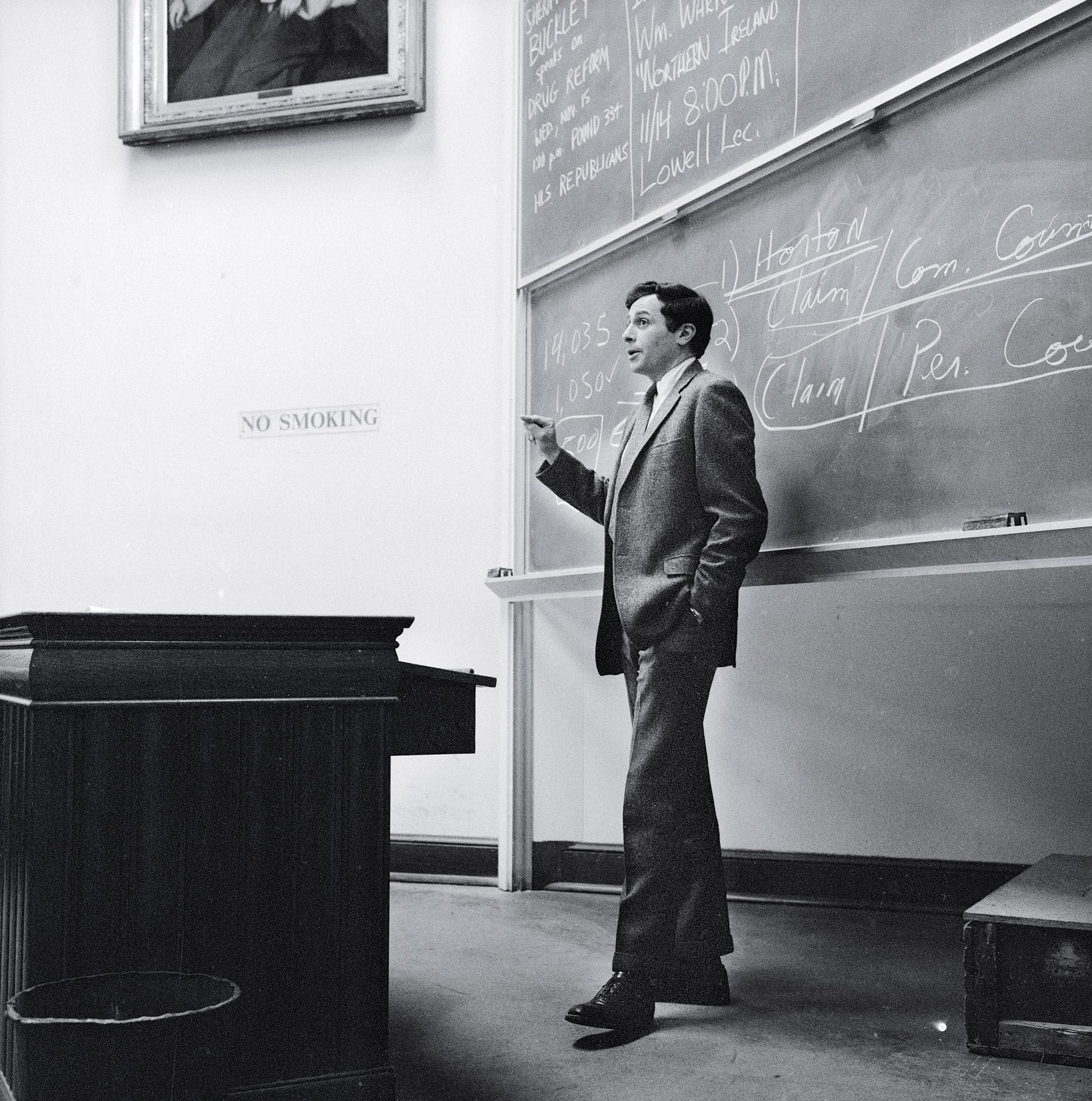 Man standing in front of a blackboard gesturing as he lectures to a class