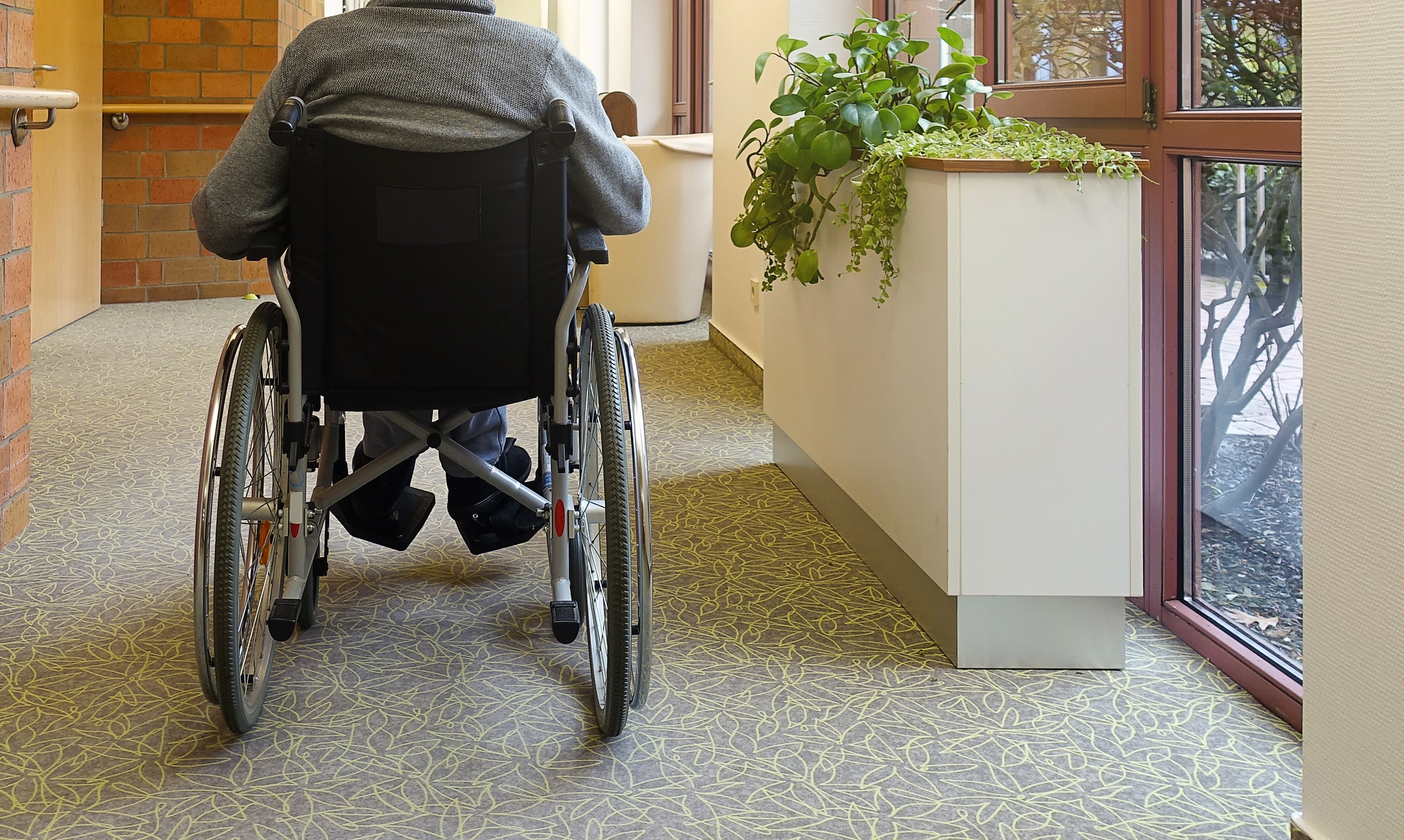 An elderly man sitting in a wheelchair in the corridor near the window