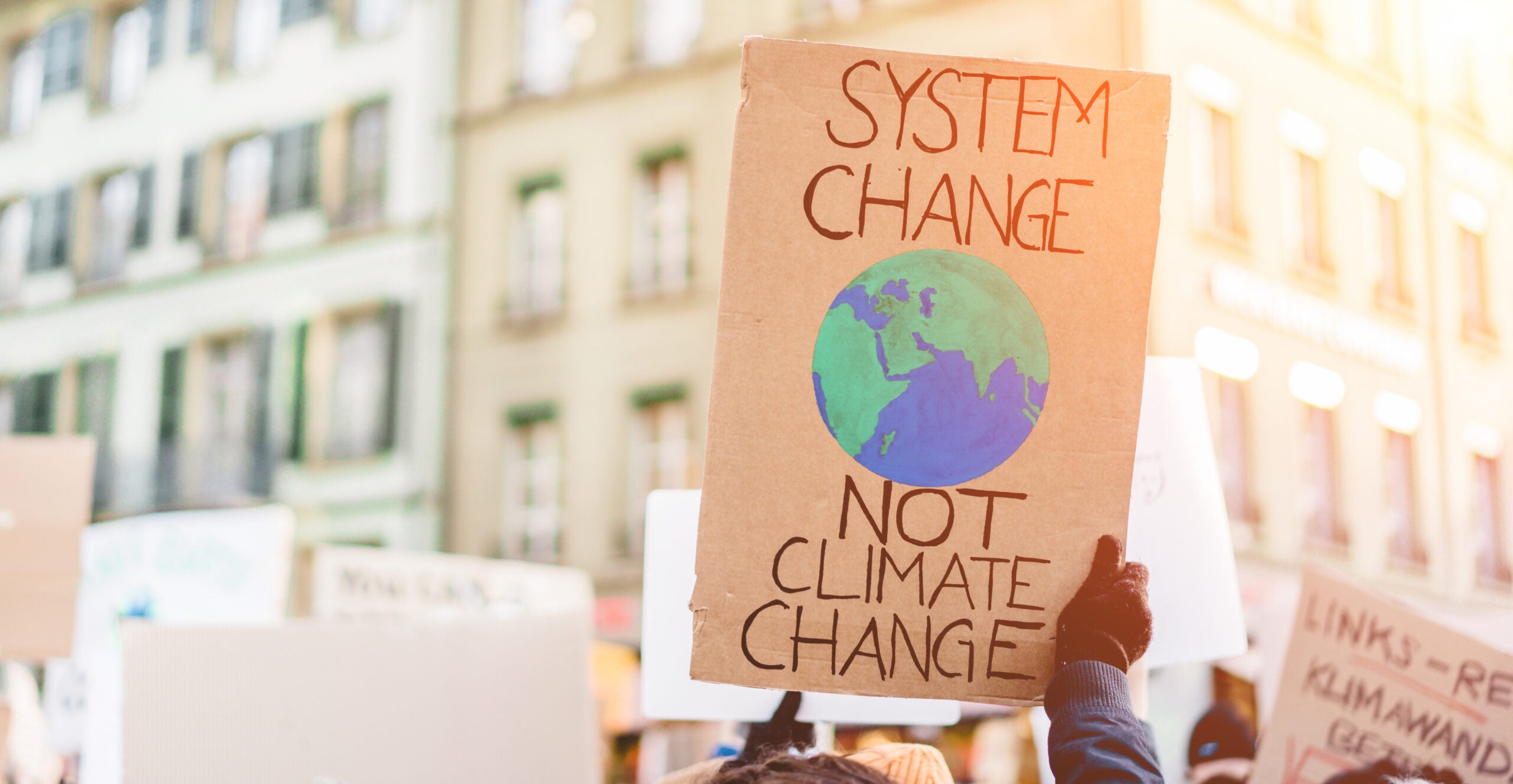 A demonstrator holding a sign the reads, System Change, Not Climate Change, with a drawing of the Earth.
