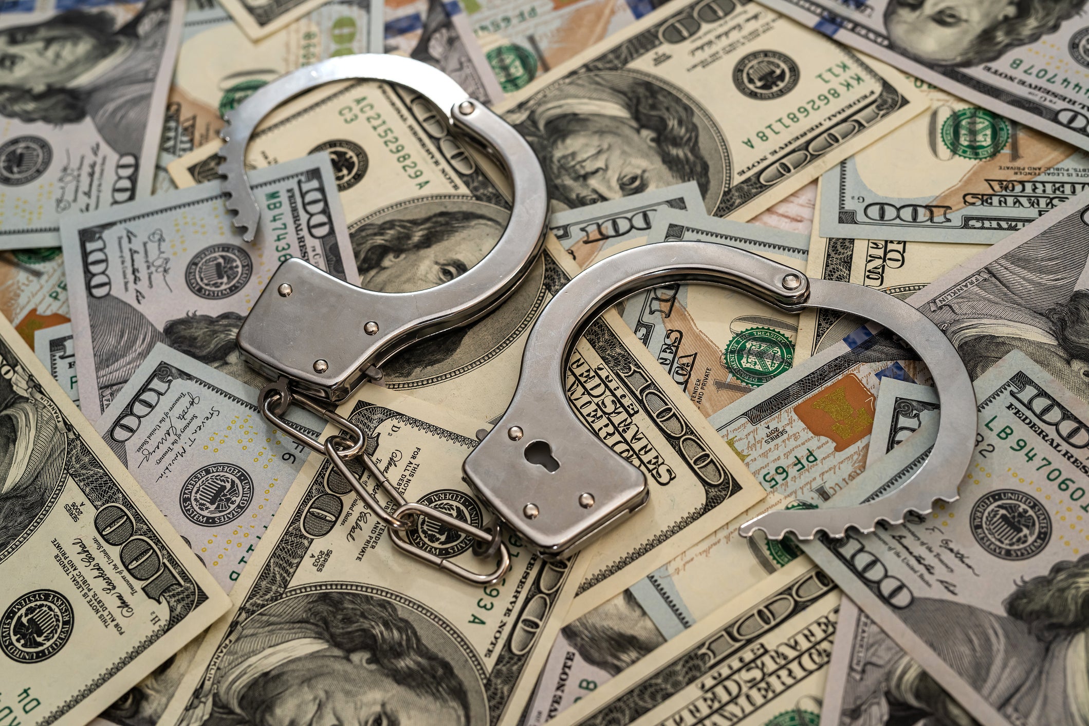 Close up of metal handcuffs on top of pile of one hundred dollar bills.