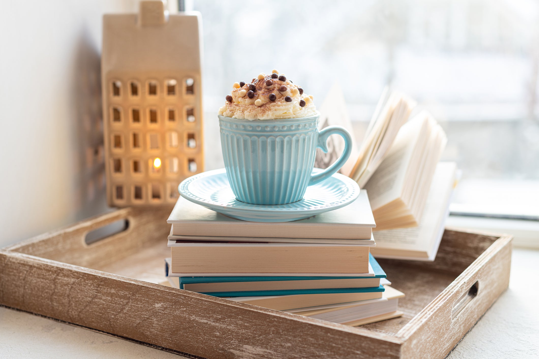 Coffee cup with whipped cream and open book on a window sill.