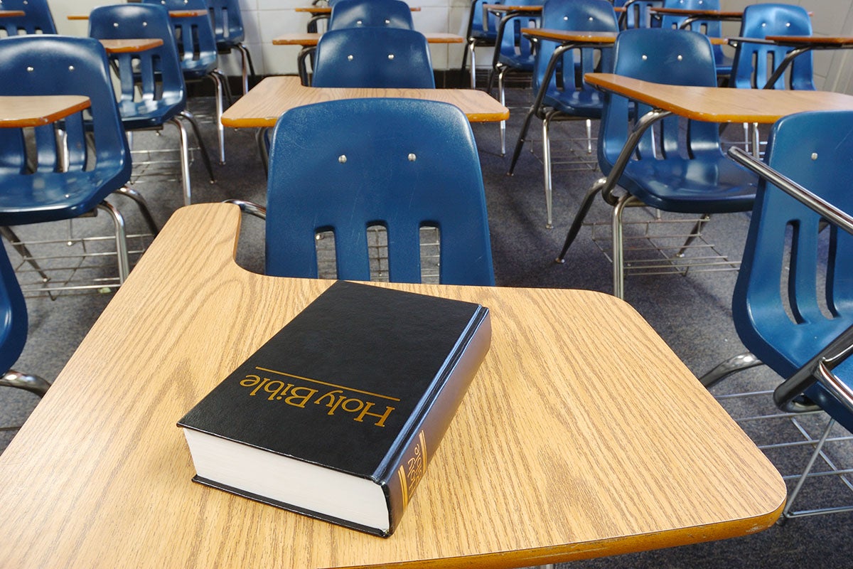 Holy Bible on a school desk, surrounded by other desks in a classroom.