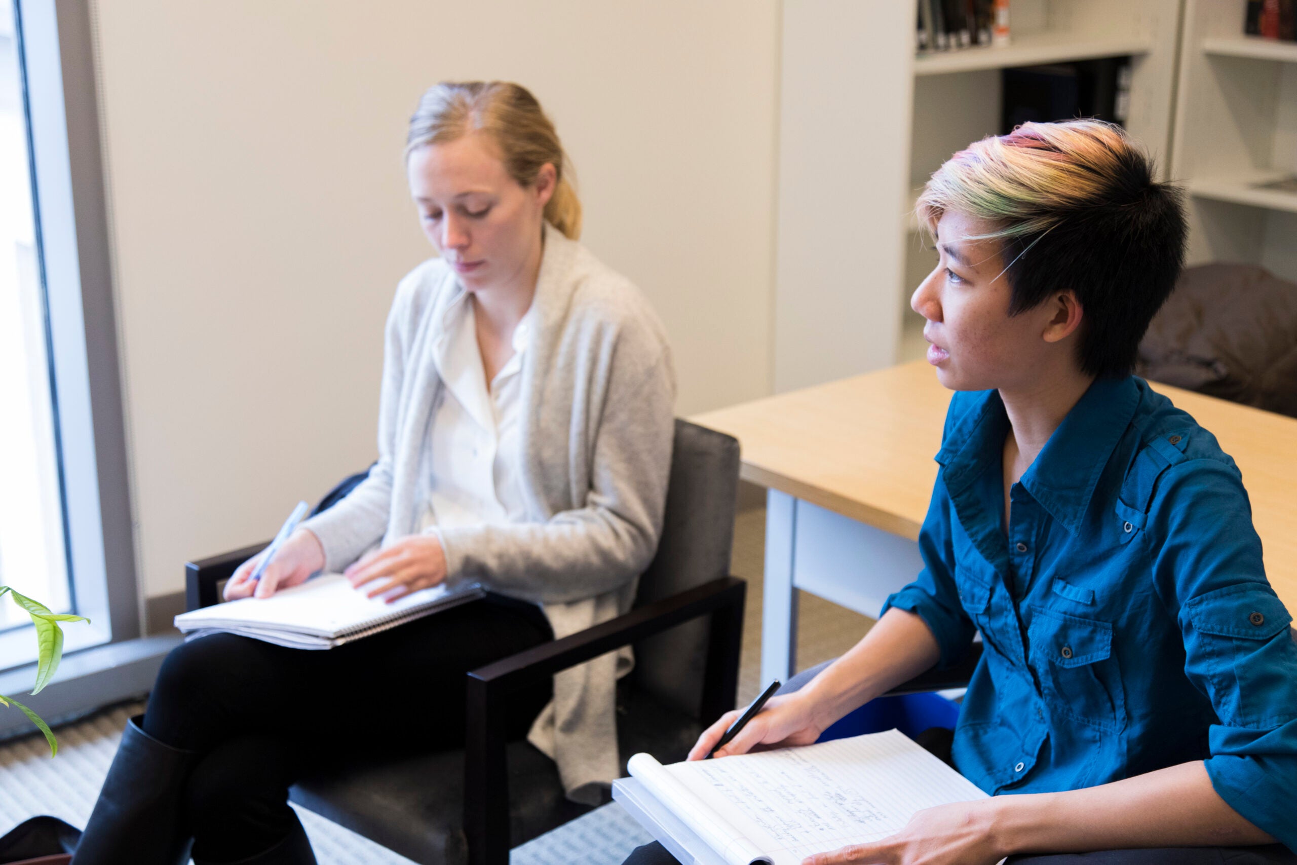 Two people sitting side by side with notebooks on their laps