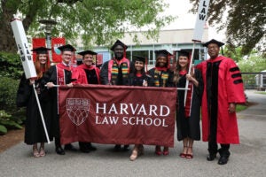 Class Marshals in commencement regalia holding a banner that says Harvard Law School pose for a group shot with Dean Manning and Dean of Students Stephen Ball