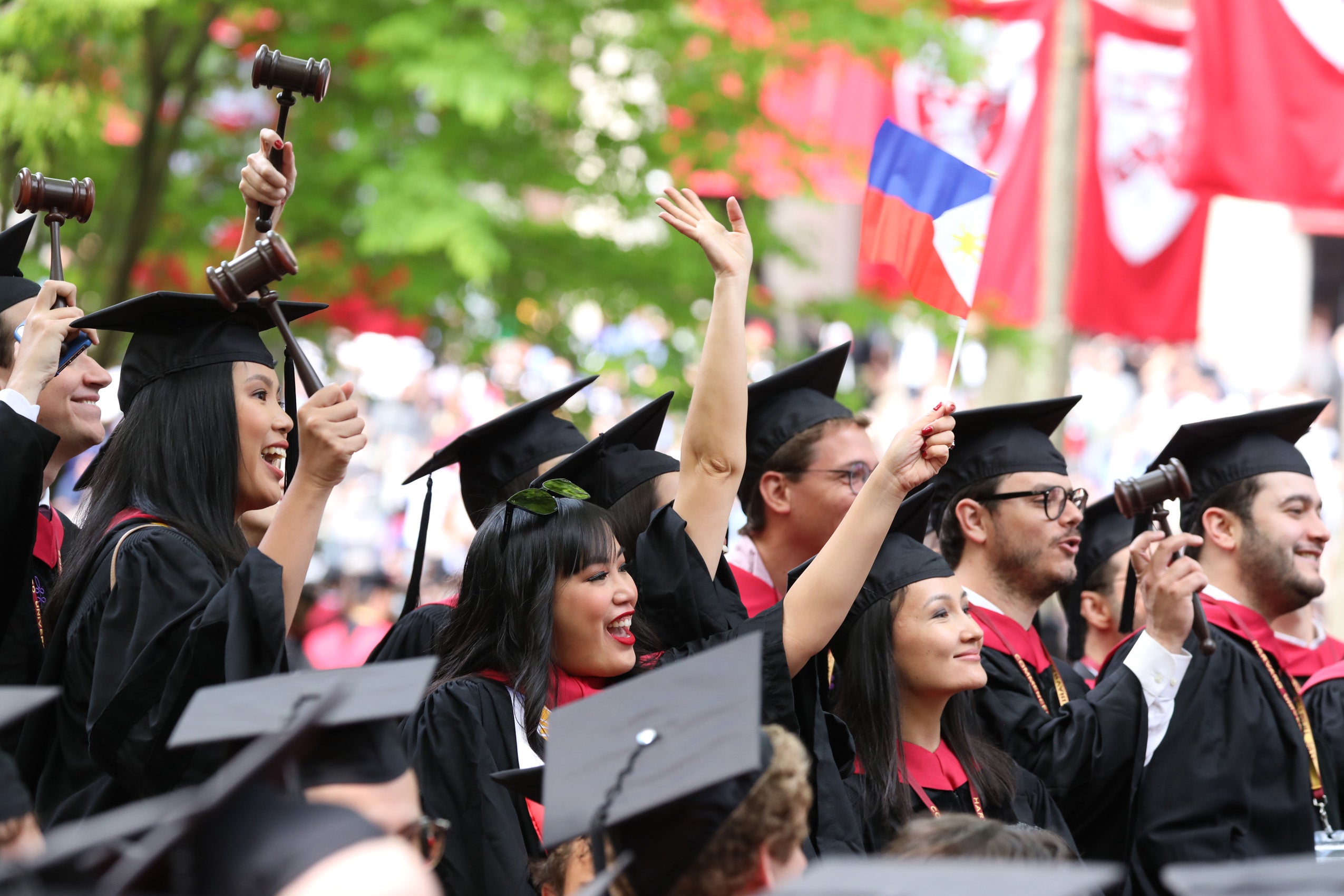 Several students in caps and gowns stand up and wave and gesture in Harvard Yard