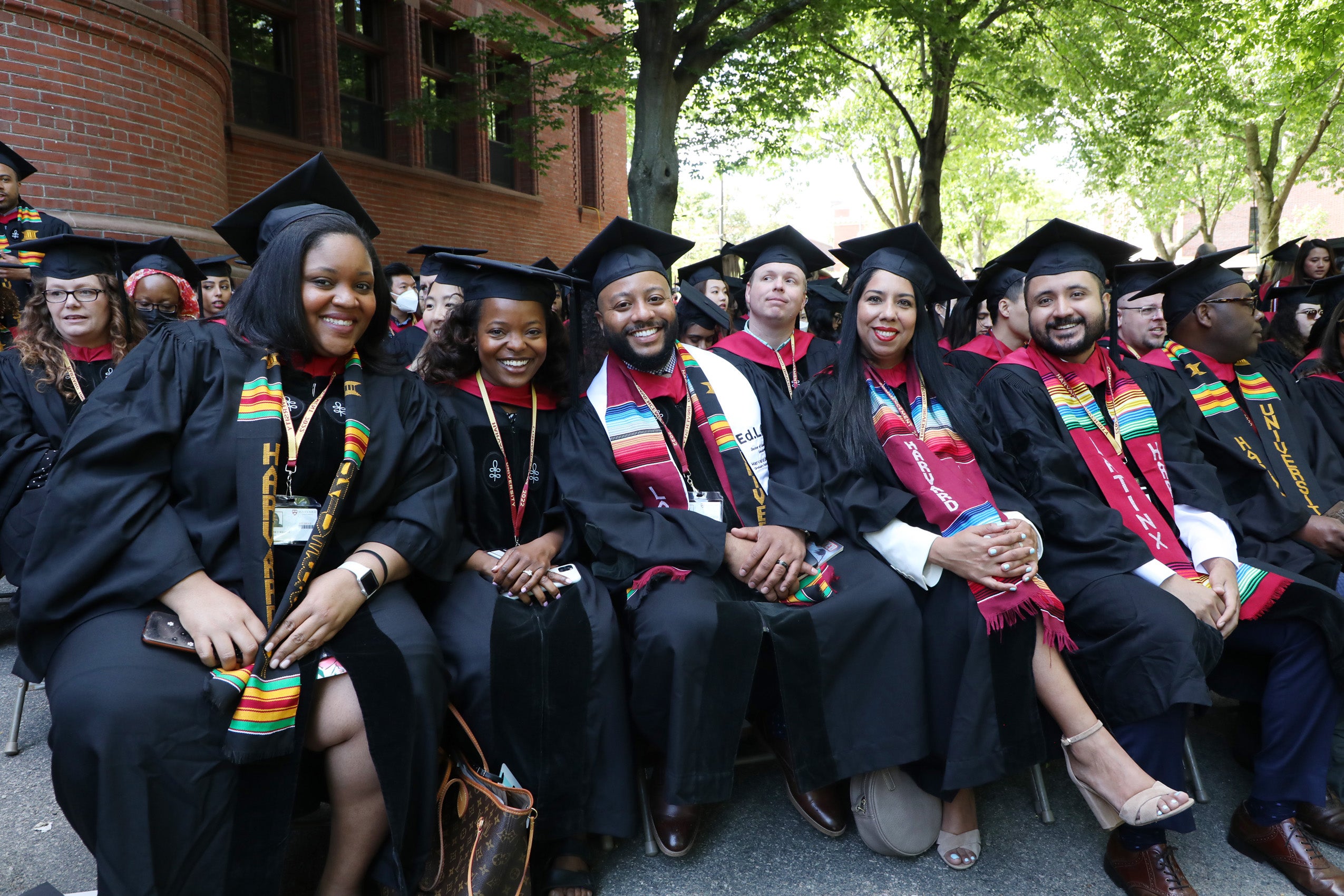A row of students in commencement regalia smile for the camera
