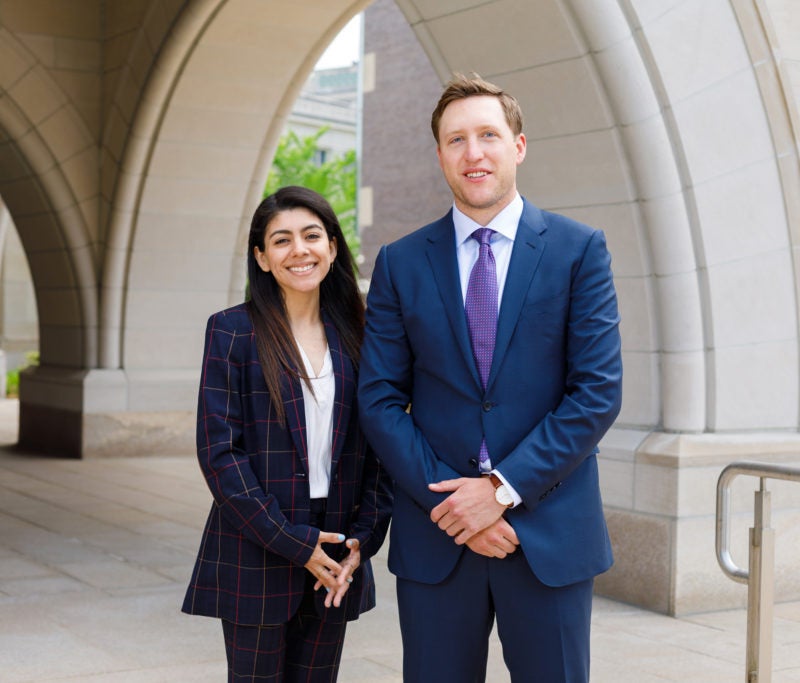 Stacey Menjivar and Henry Beshar, wearing blue blazers, stand outside a building on the Harvard Law School campus.