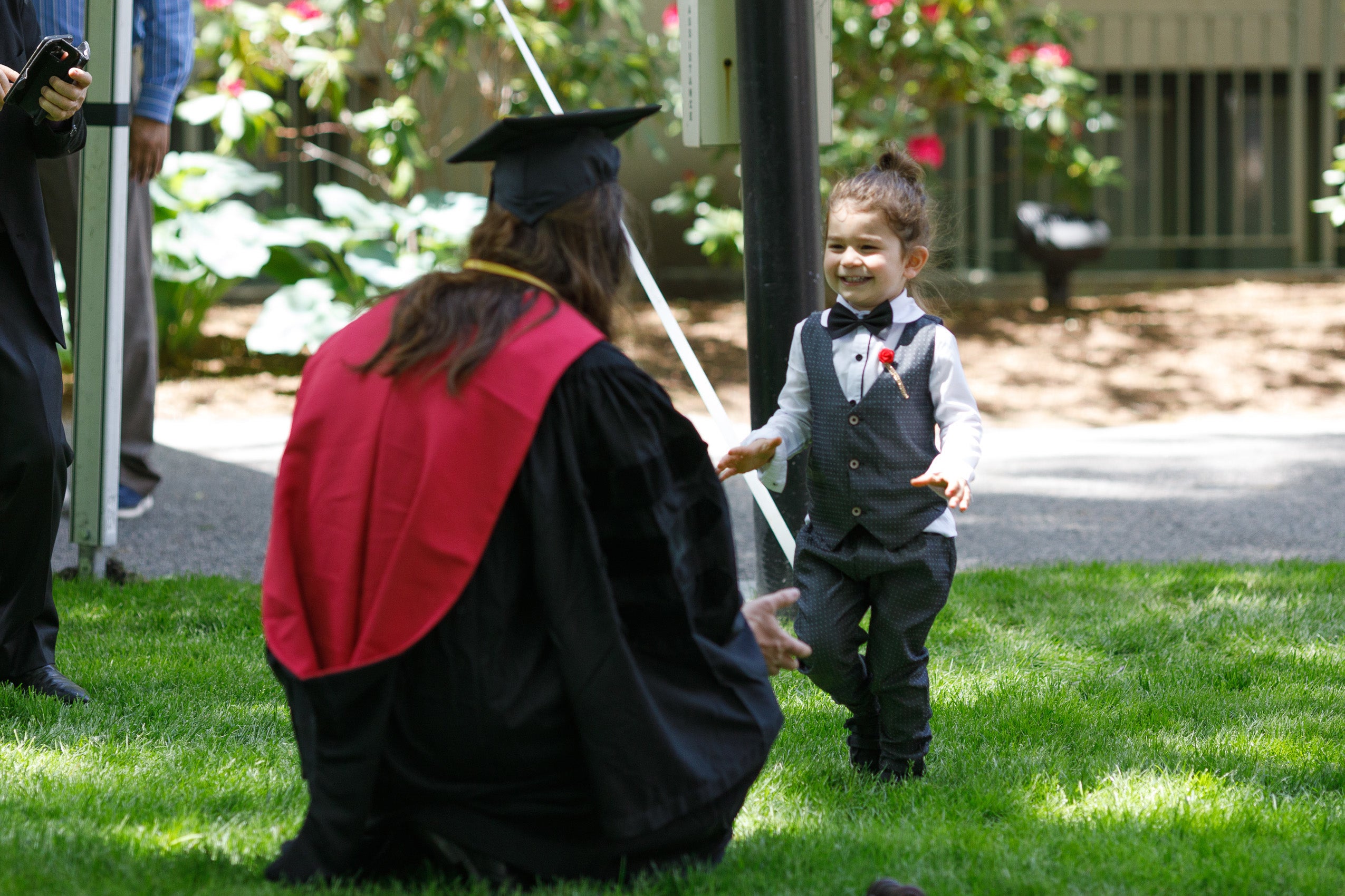 A young boy dressed up for a special occasion runs up to a women wearing a cap and gown