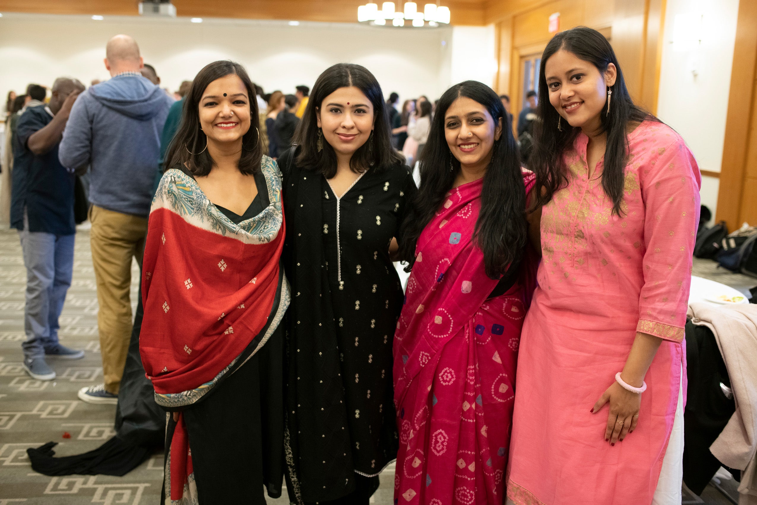 Four international graduate students dressed in clothing worn in their country pose for a photo at an event.