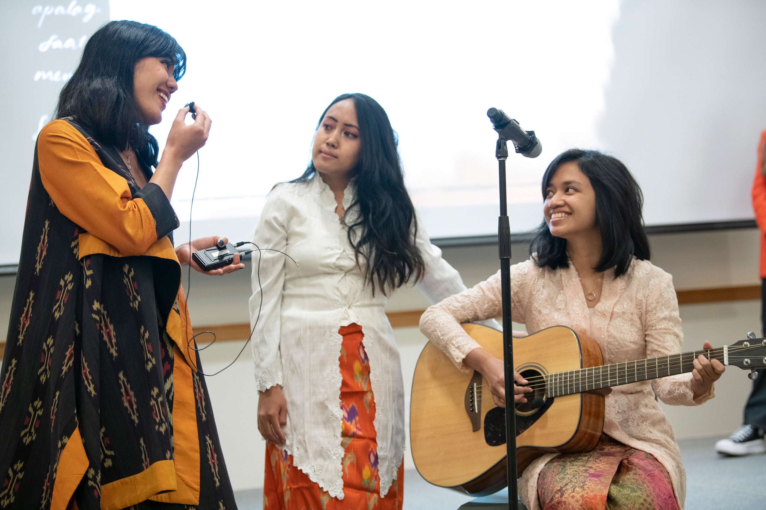 Three female graduate students sing and play guitar at an event