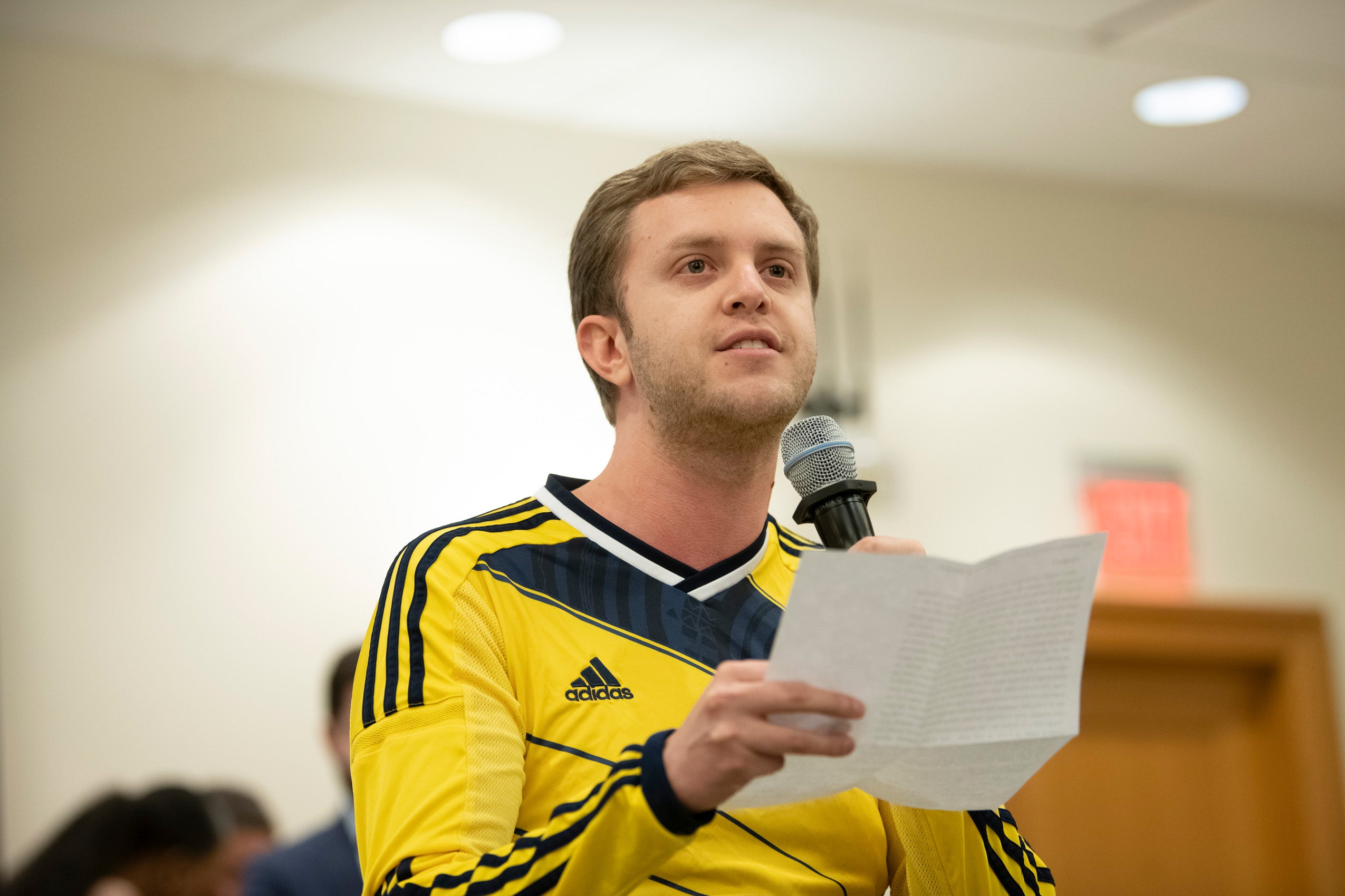 A graduate student wearing yellow shirt addresses the students gathered at an event
