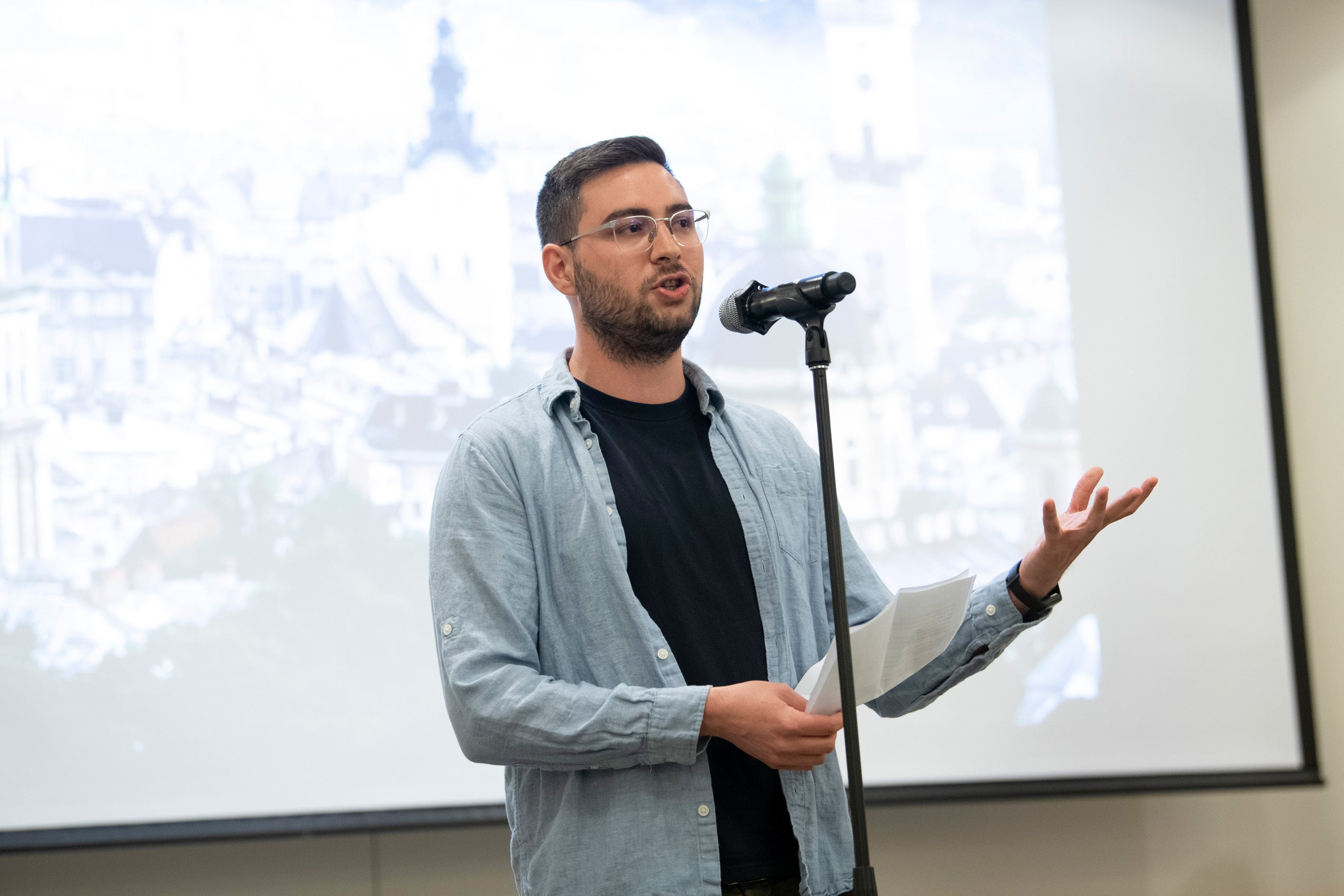 A student stands at a microphone with some papers in his hands and reads to the audience