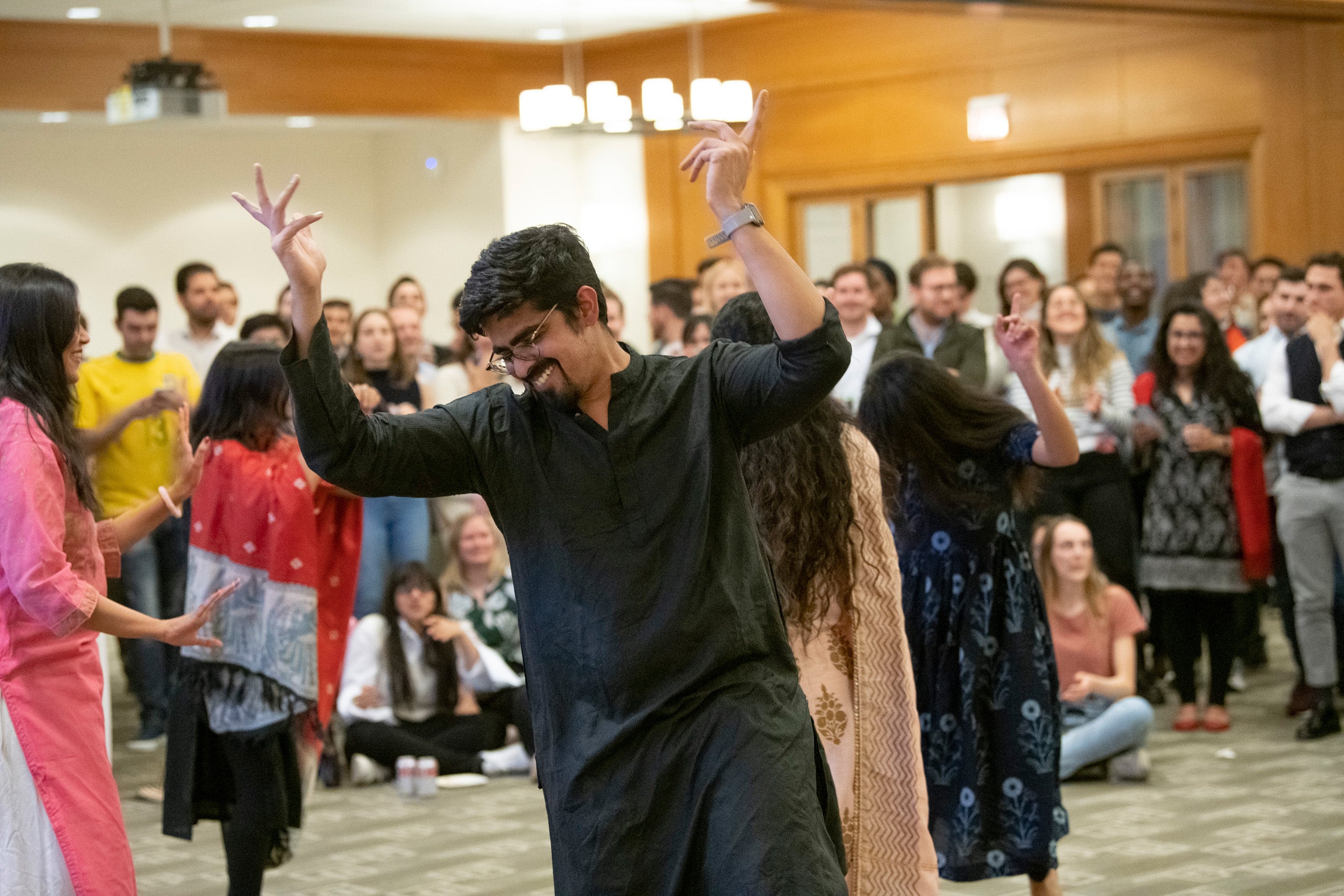A graduate student participates in a dance performance in front of a large crowd of classmates.