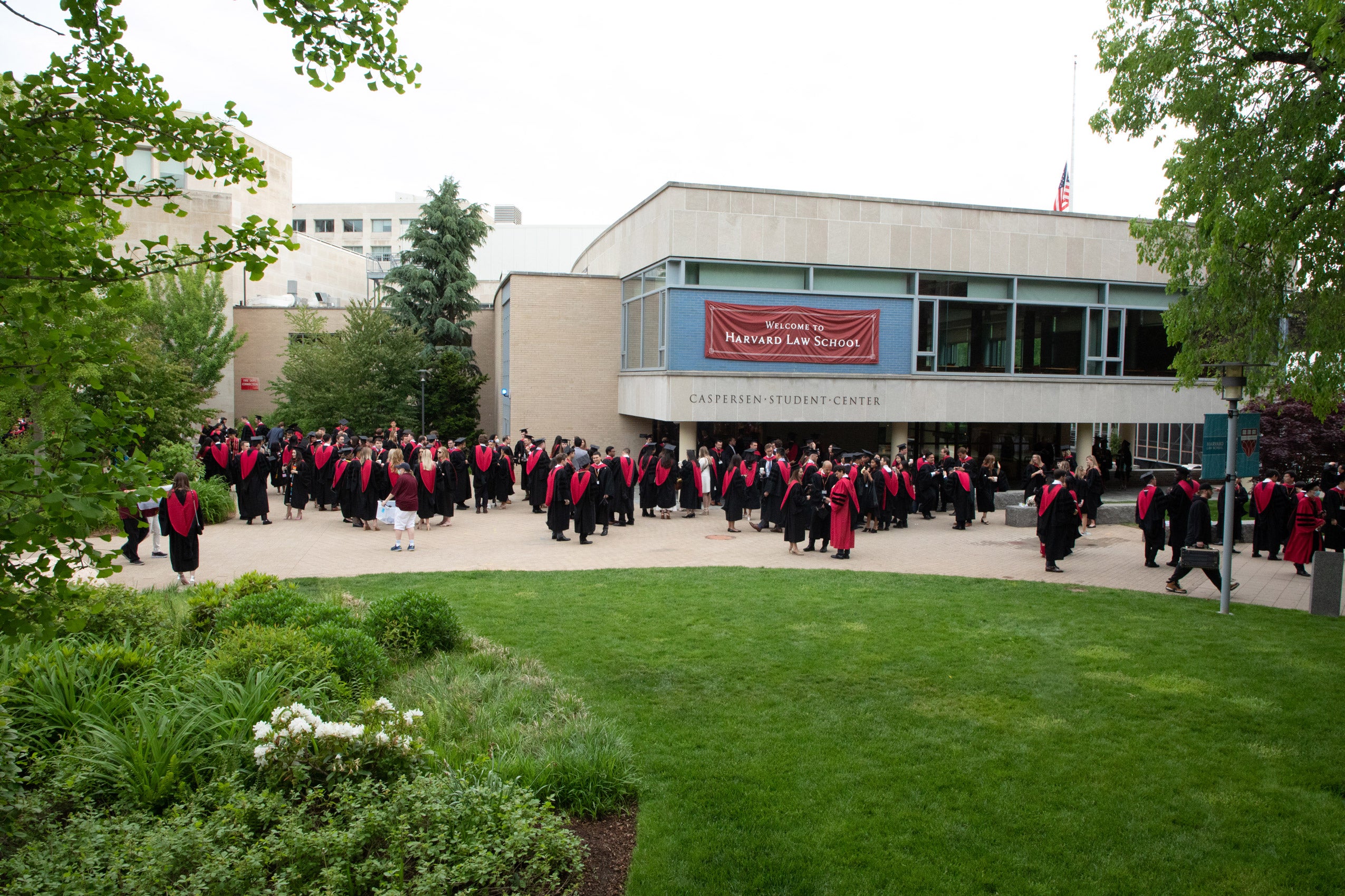 A wide shot of graduates wearing caps and gowns standing in front of a student center and below a sign that says