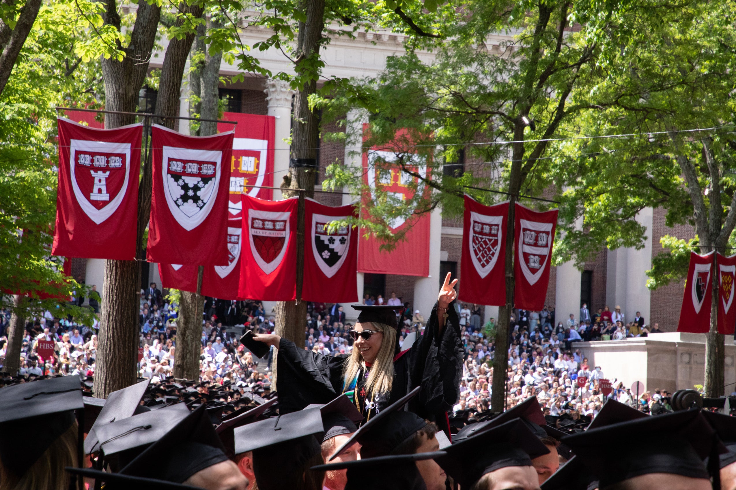 A graduate pops up above a sea of caps in Harvard Yard waving her arms out to the side