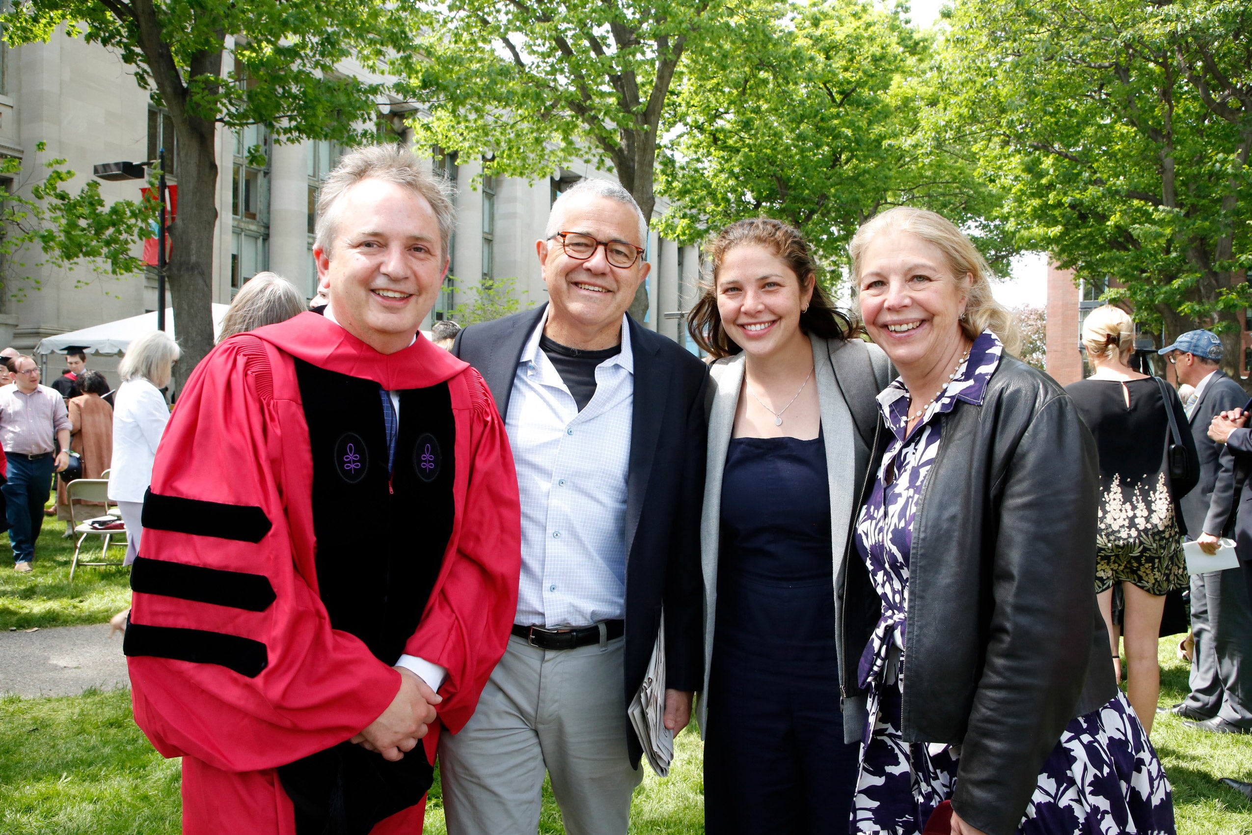 A family poses with a professor wearing commencement regalia on Holmes Field