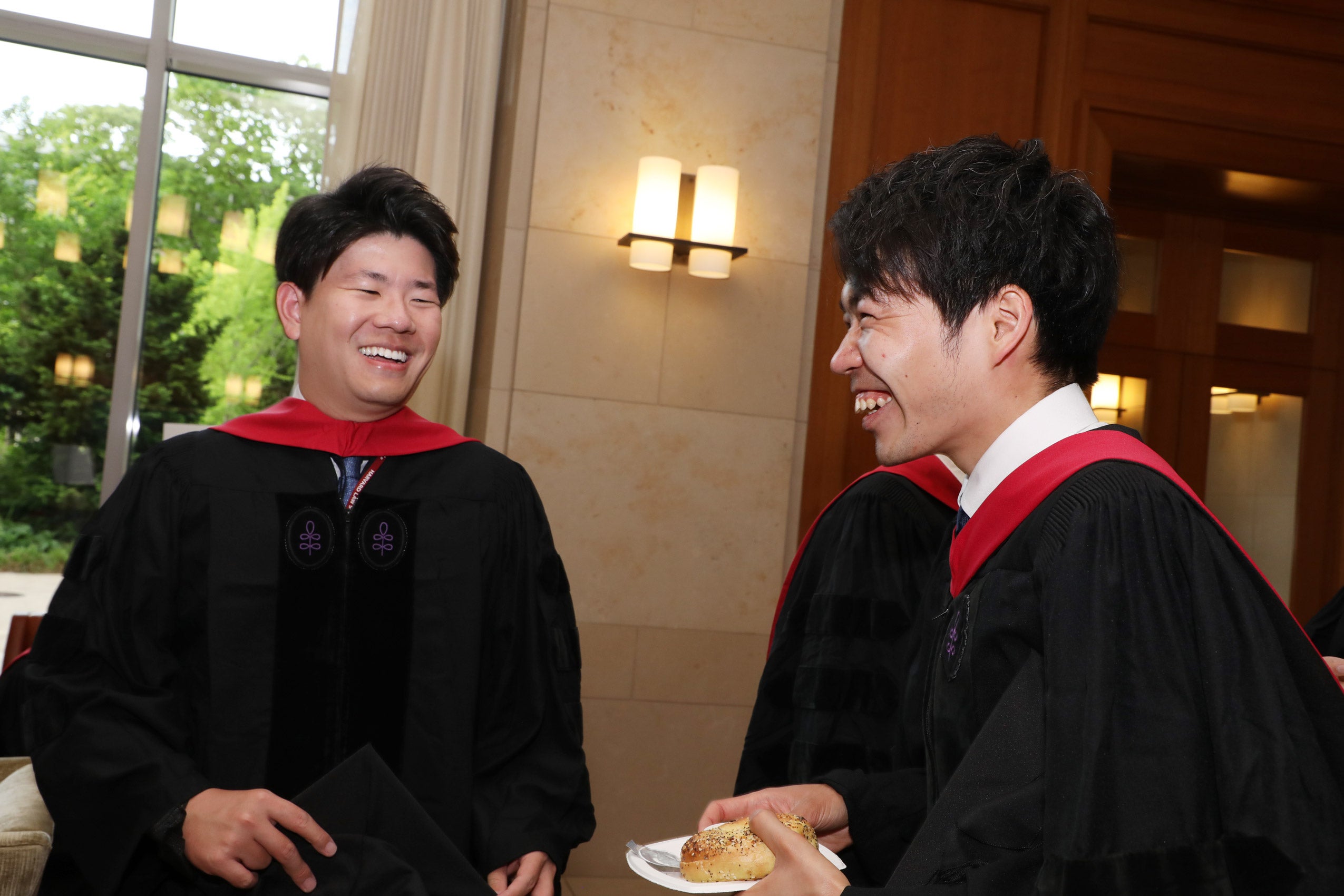 Two men wearing caps and gowns share a light moment