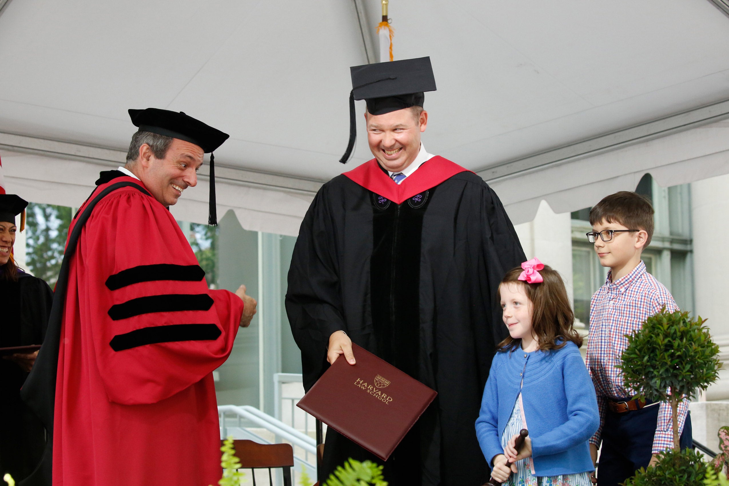 Two young children with their father as he is getting his diploma from the dean