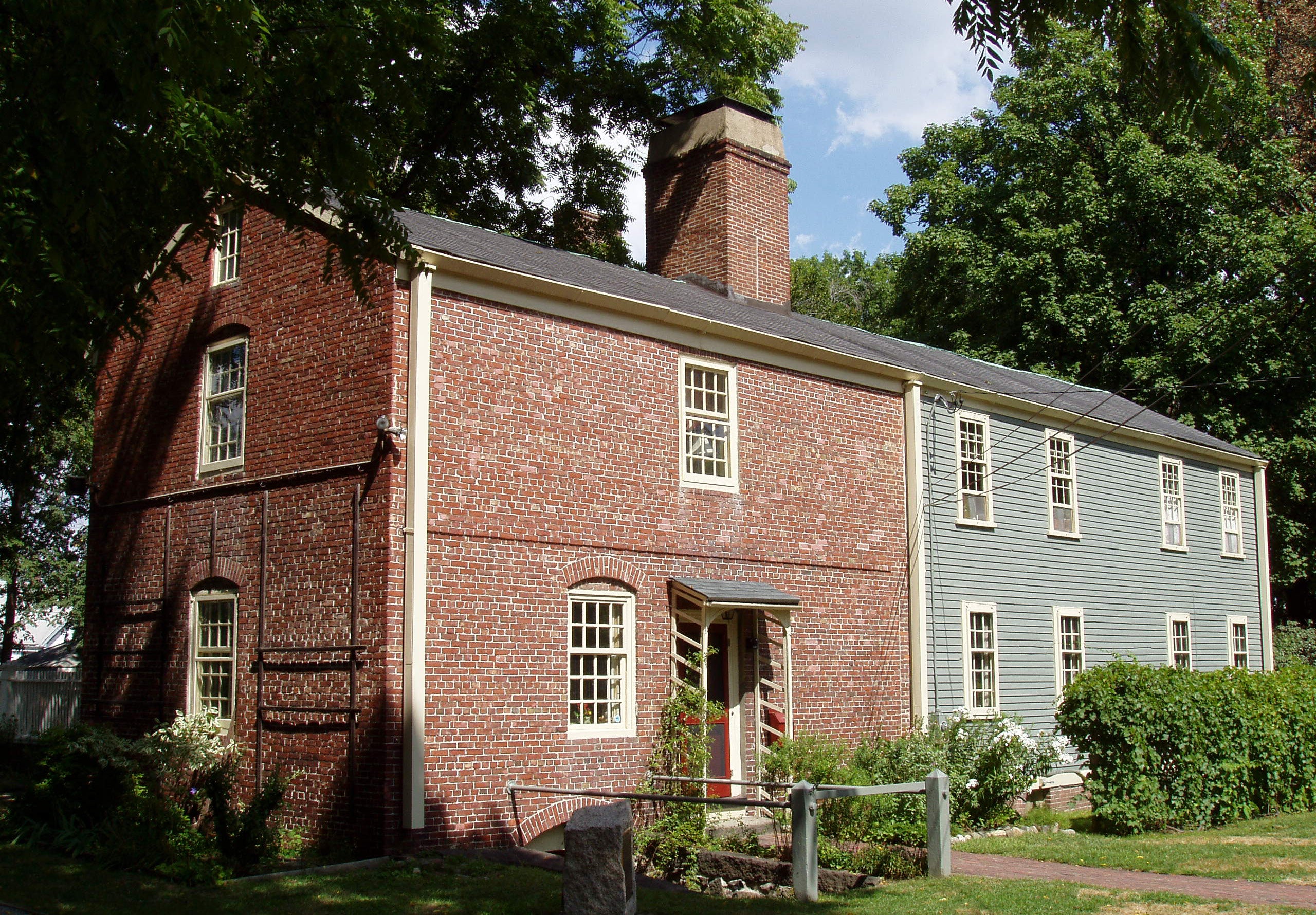 A brick building with two windows and and door and a light green building with 8 windows under one roof.