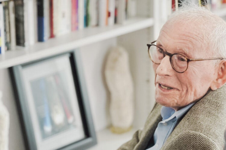 An elderly man sitting in a chair smiles as he looks off to the left
