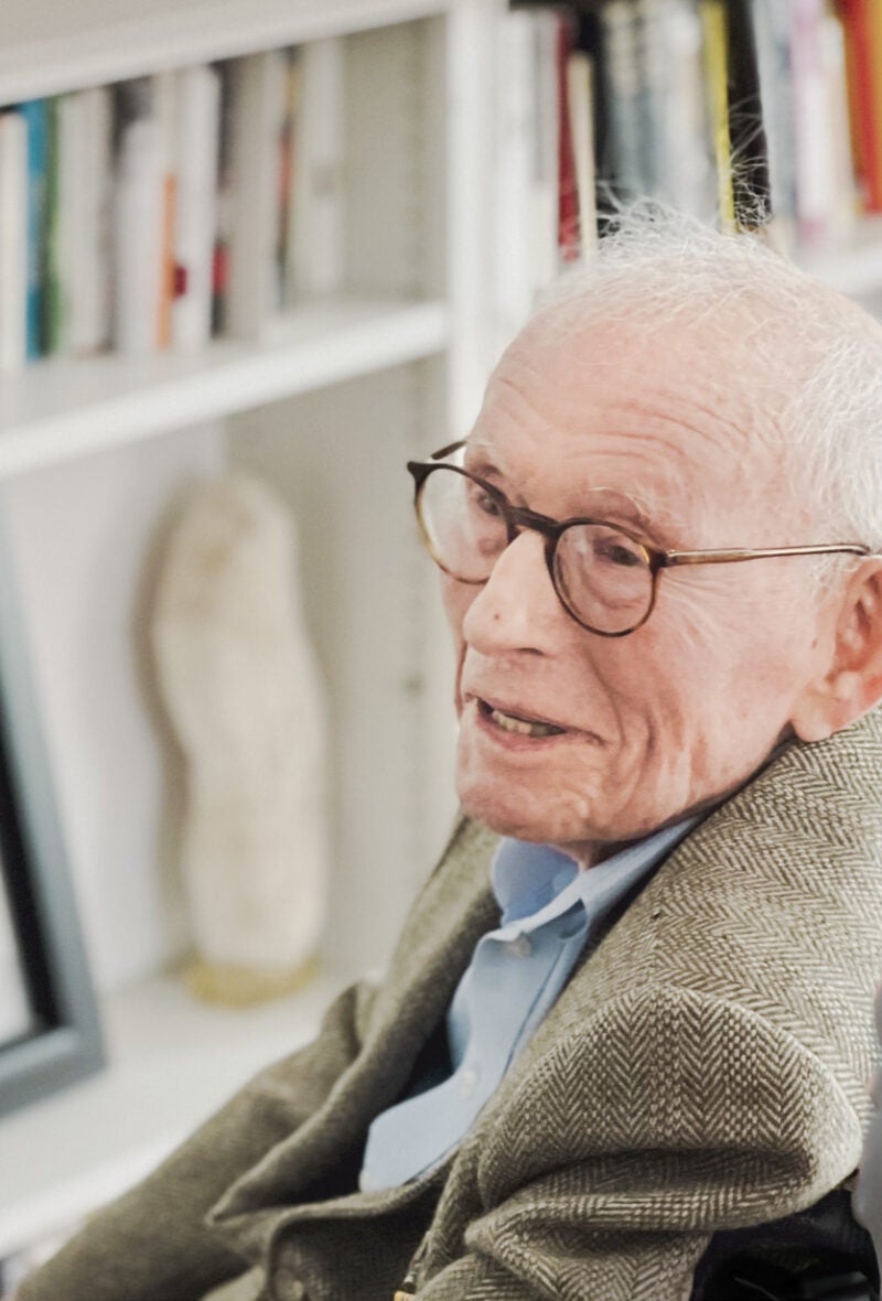 An elderly man sitting in a chair smiles as he looks off to the left