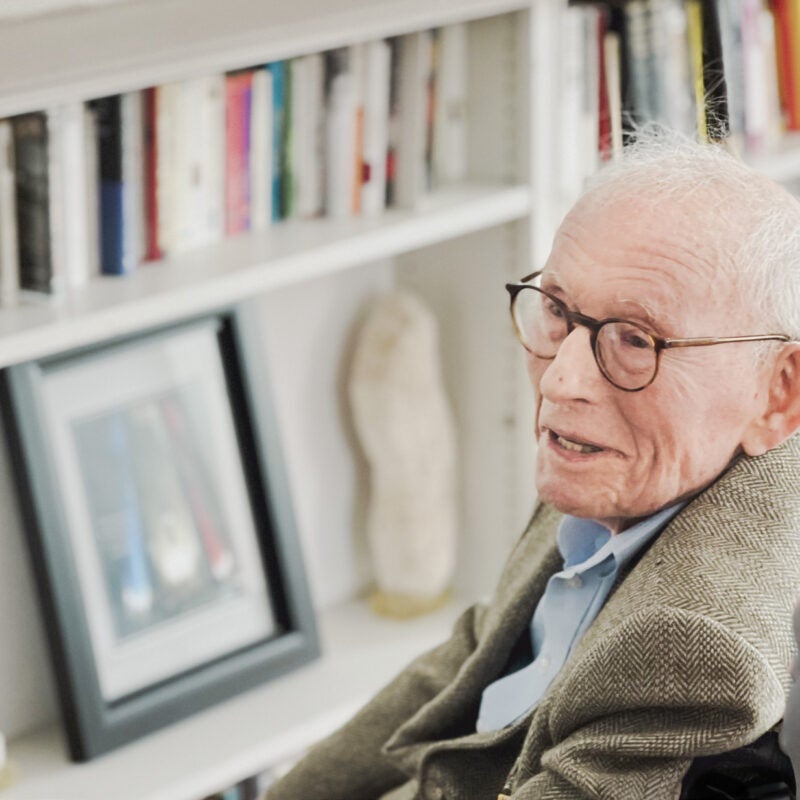 An elderly man sitting in a chair smiles as he looks off to the left