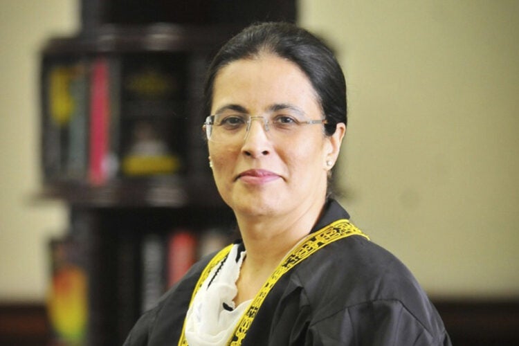 A woman in a black robe with yellow embroidered trim poses for a portrait