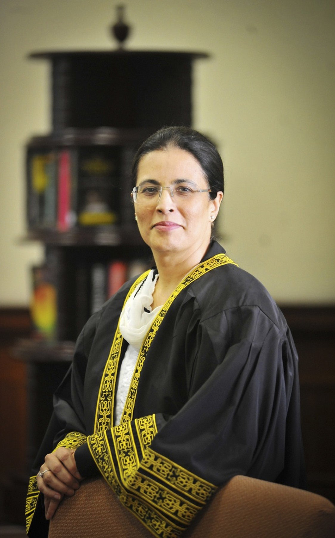A woman in a black robe with yellow embroidered trim poses for a portrait