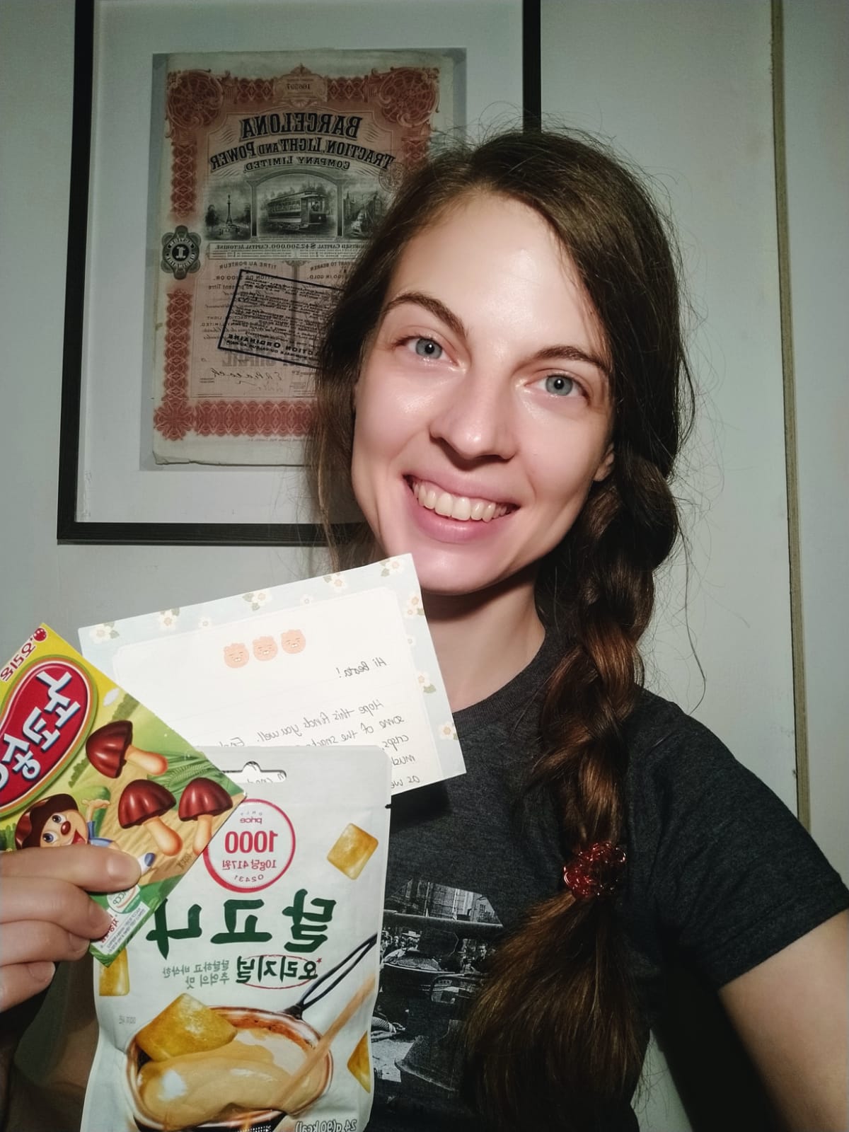 Woman standing, holding a notecard and two bags of snacks from South Korea.