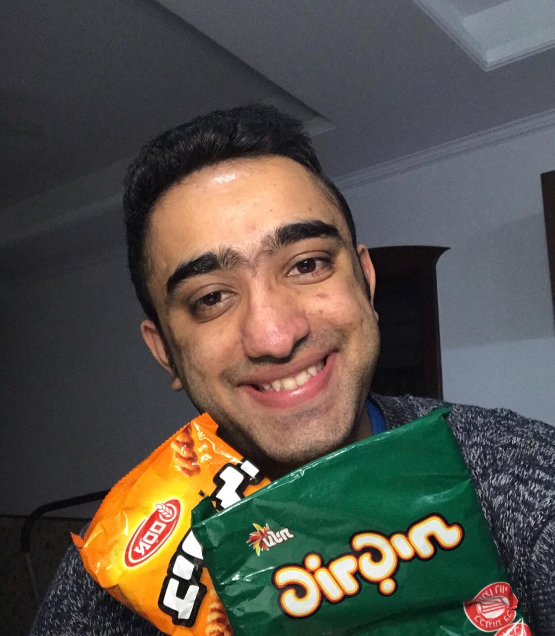 A man posing with two bags of snacks.