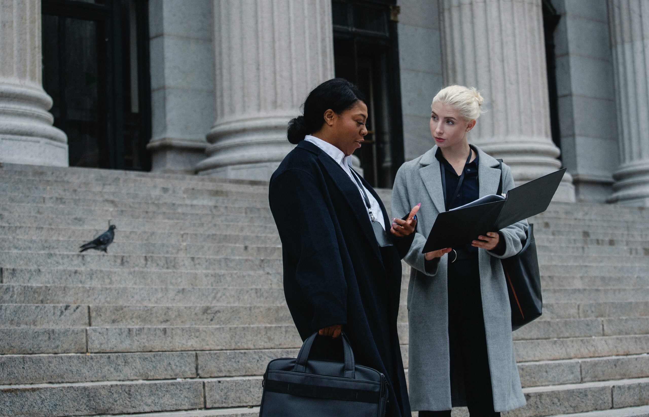 Two professional women reviewing a file on outdoor steps