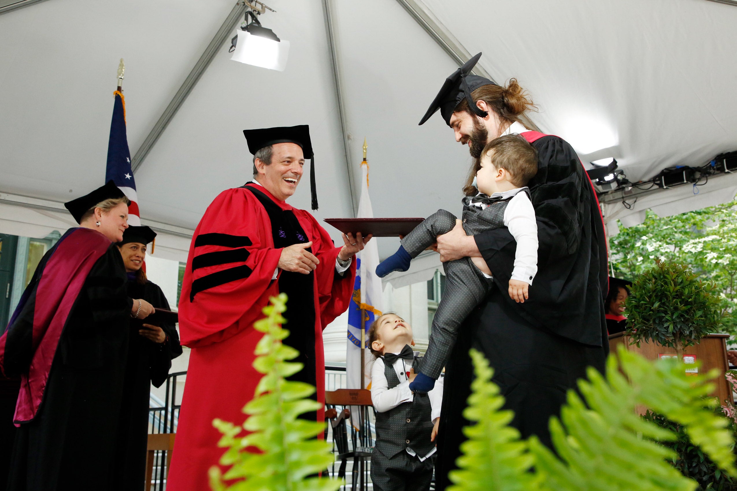 A graduate with his two young boys on the stage getting his degree from the dean