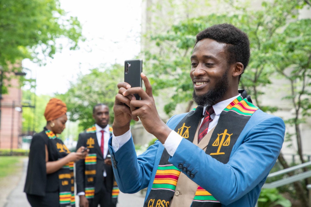 A man wearing a Commencement scarf looks at his cell phone
