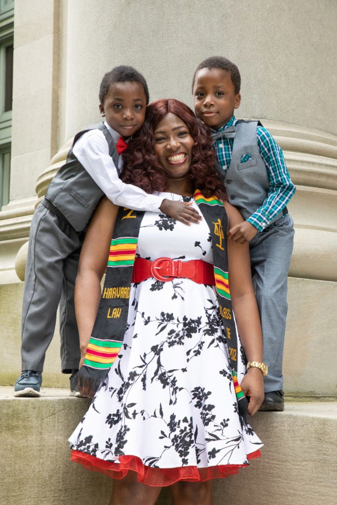 A woman wearing wearing a graduation scarf gets hugs from two young boys