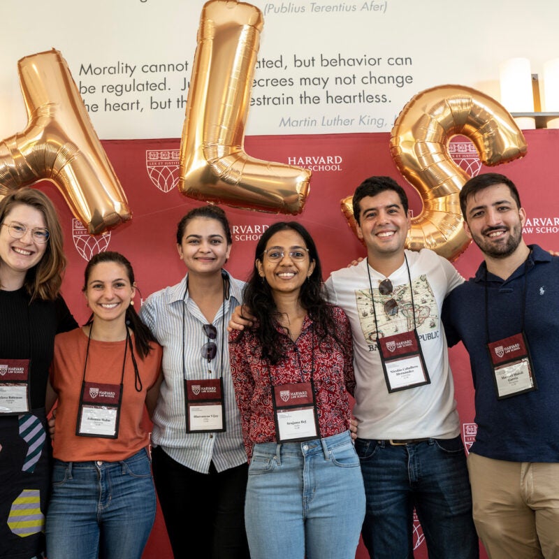 A group of LL.M. students pose in front of a back drop and gold HLS balloons