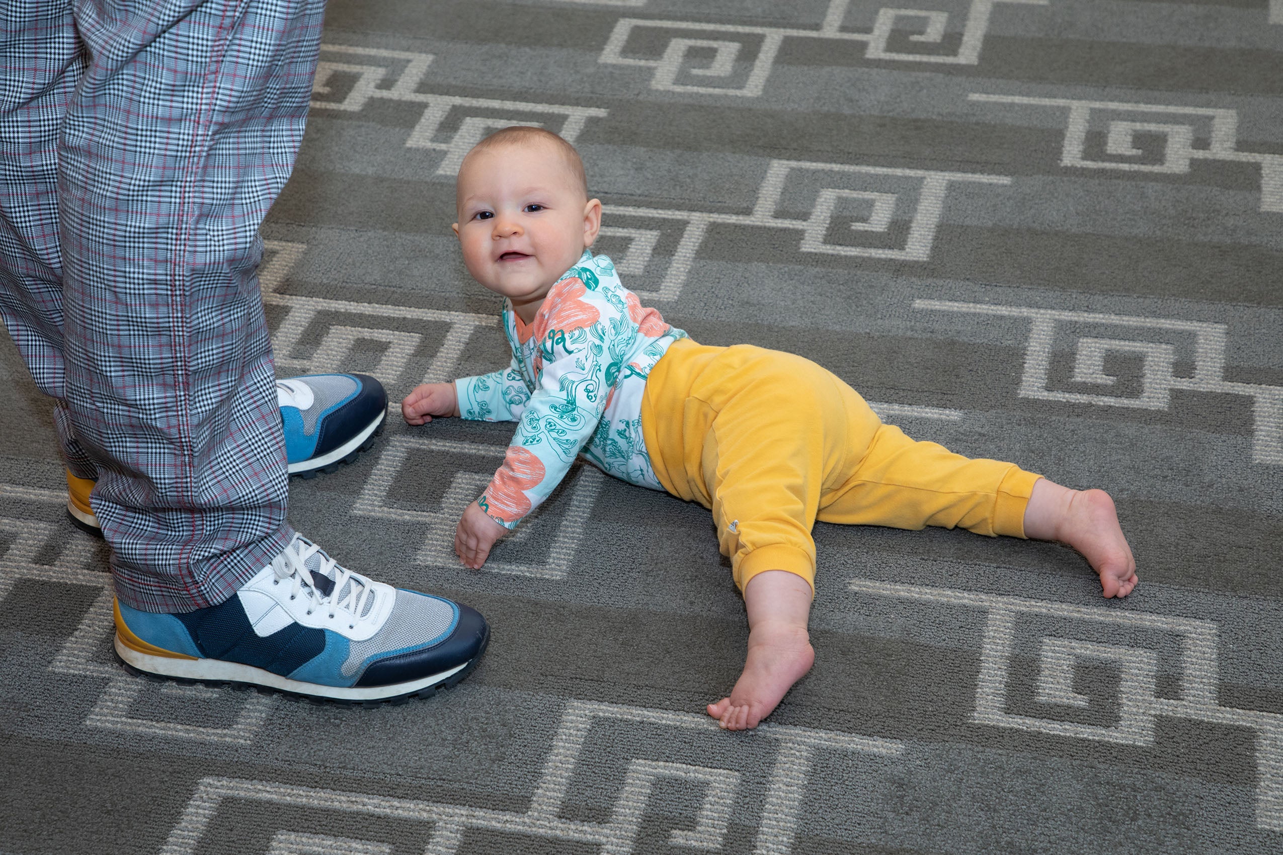 A baby laying on its stomach on the floor looking up and smiling.