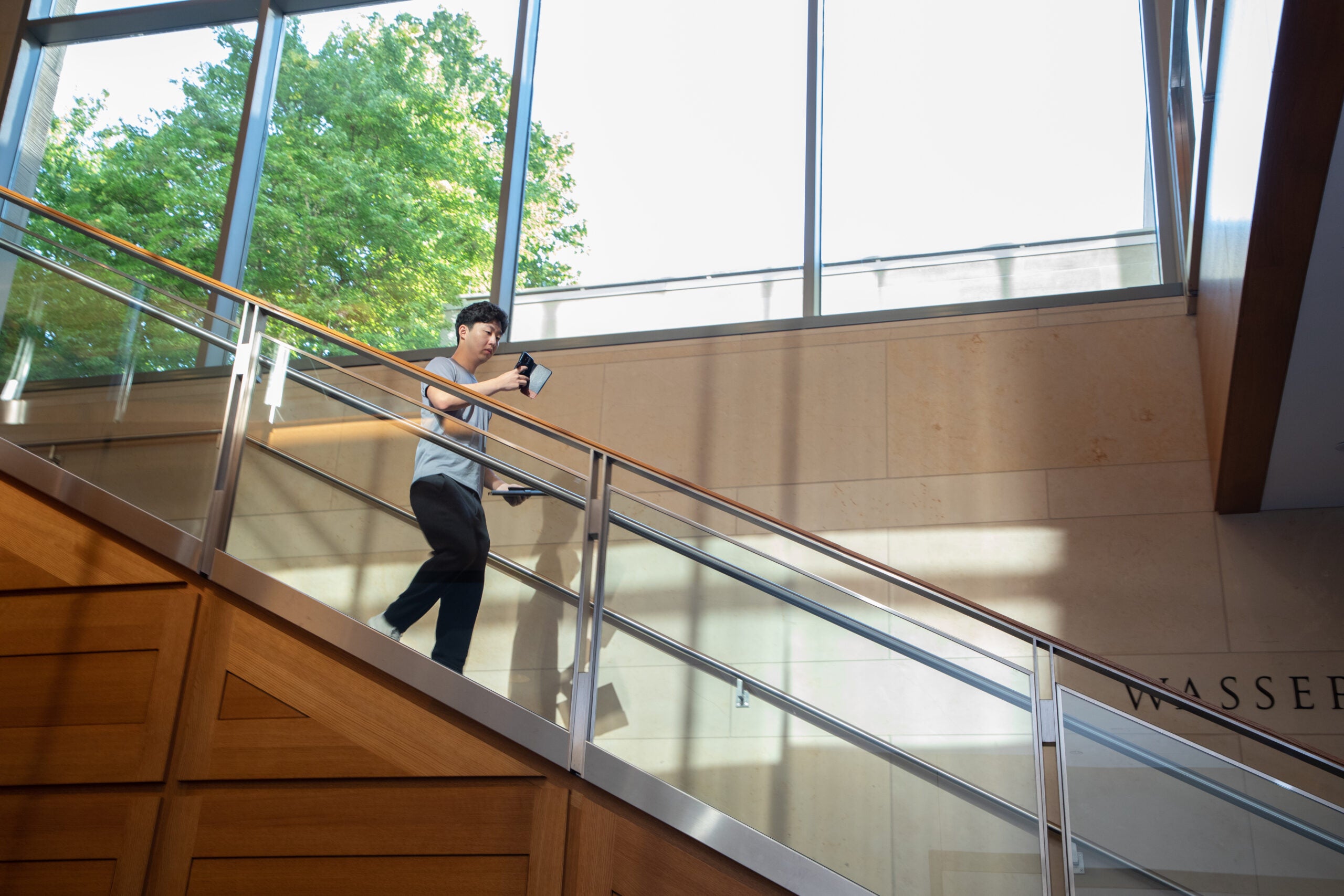 A student walking down a staircase while looking at his phone.